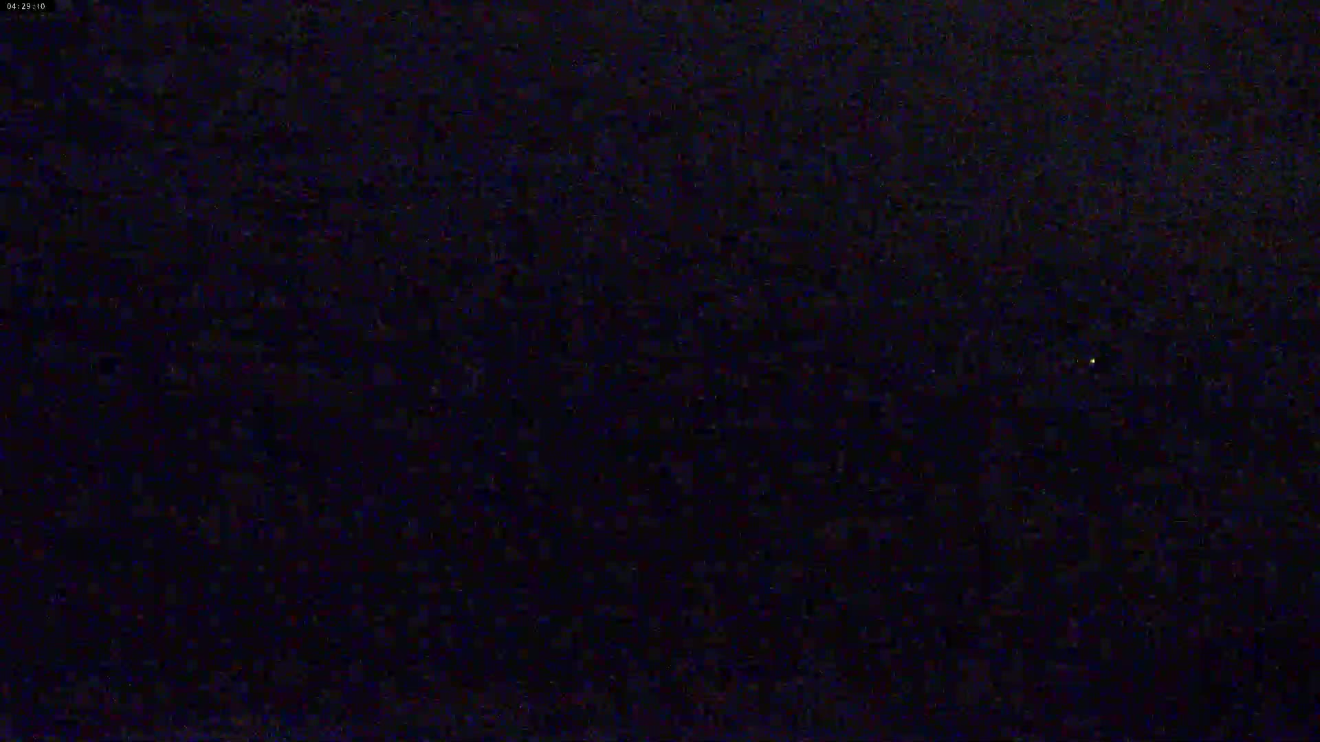 A dark, nighttime scene shows a very small, faint, yellow light in the center.