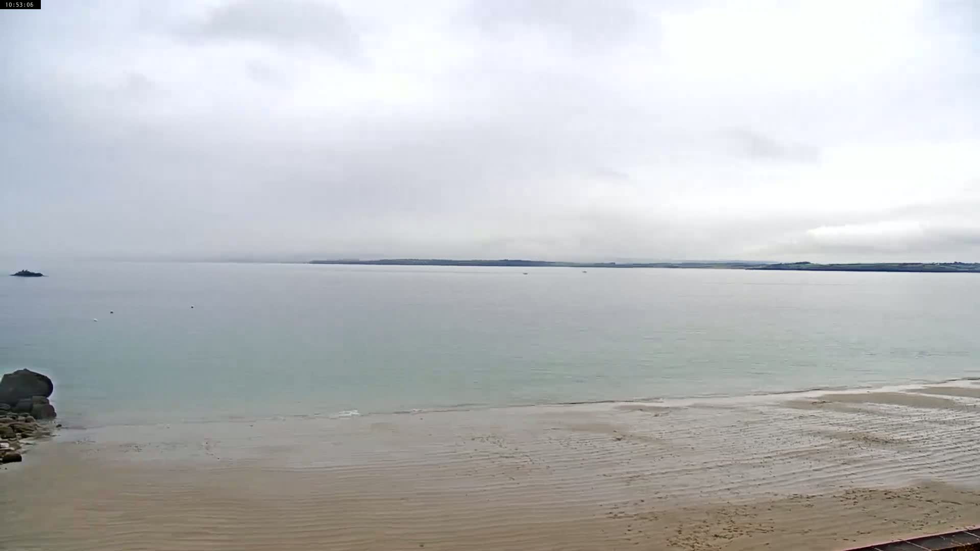 A wide sandy beach stretches to a calm, light-green sea under an overcast sky.