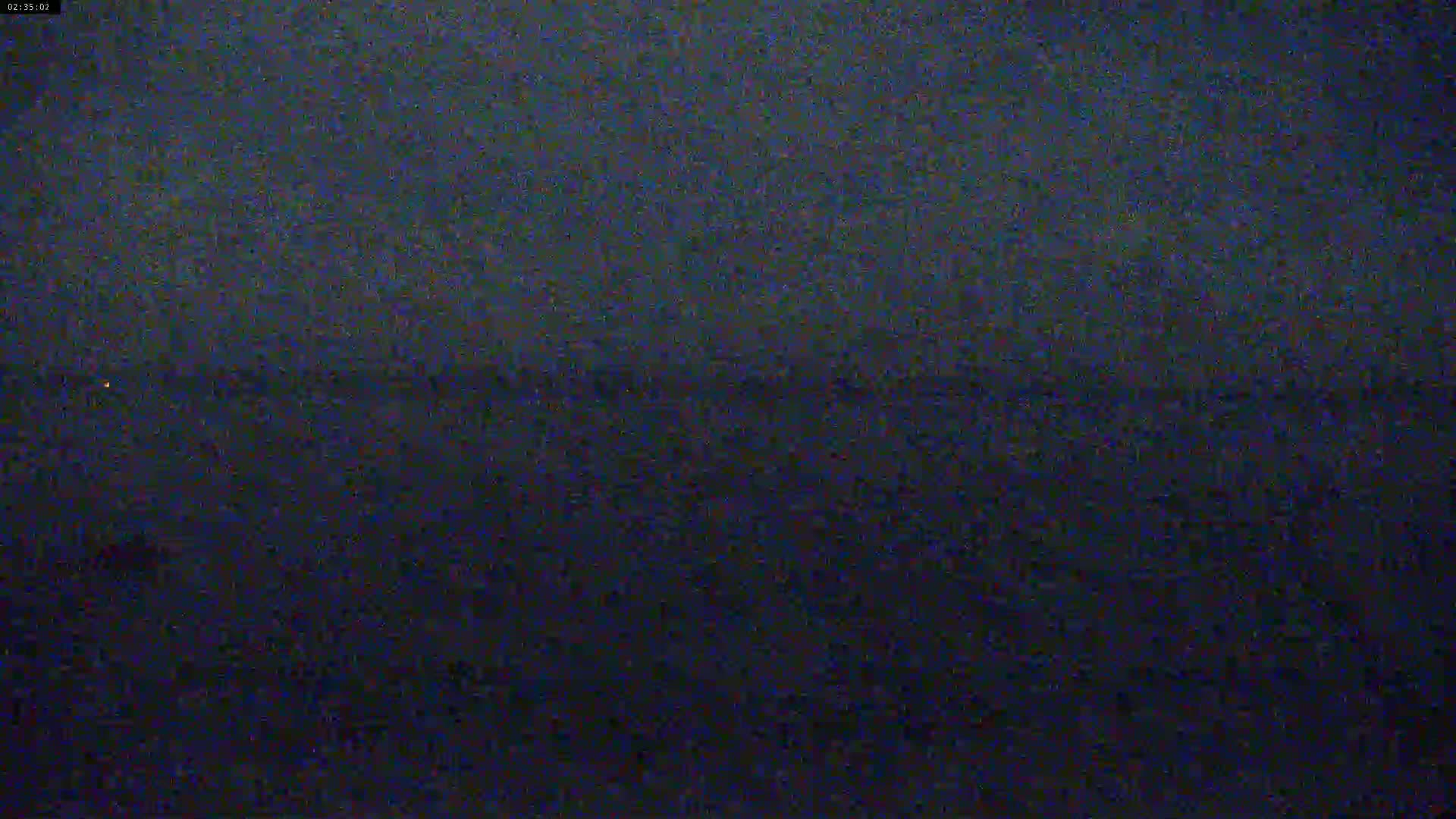 A dark, nighttime view of a mostly featureless body of water under a cloudy sky.