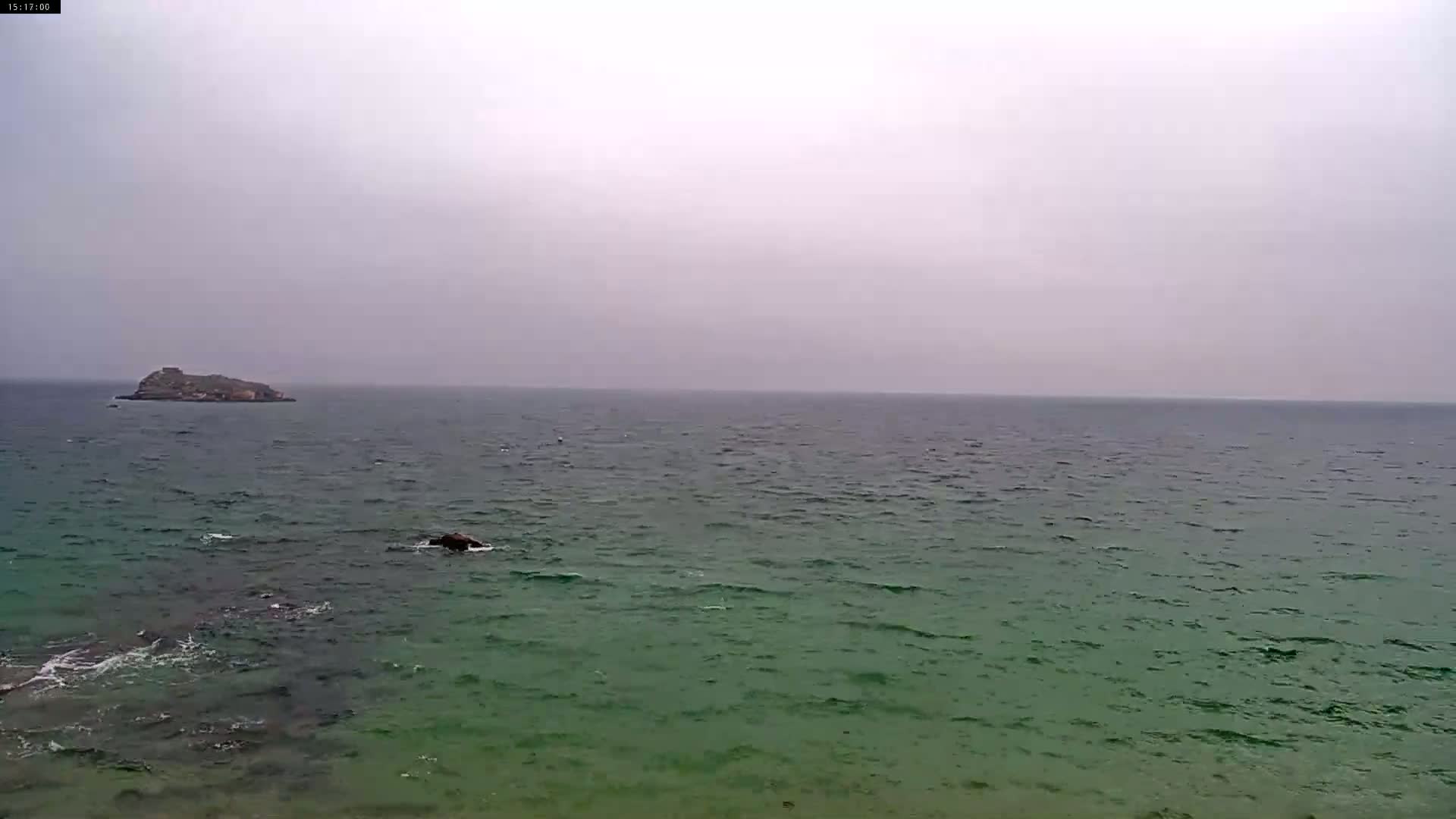 A small island is visible in the distance across a green-tinged sea under an overcast sky.