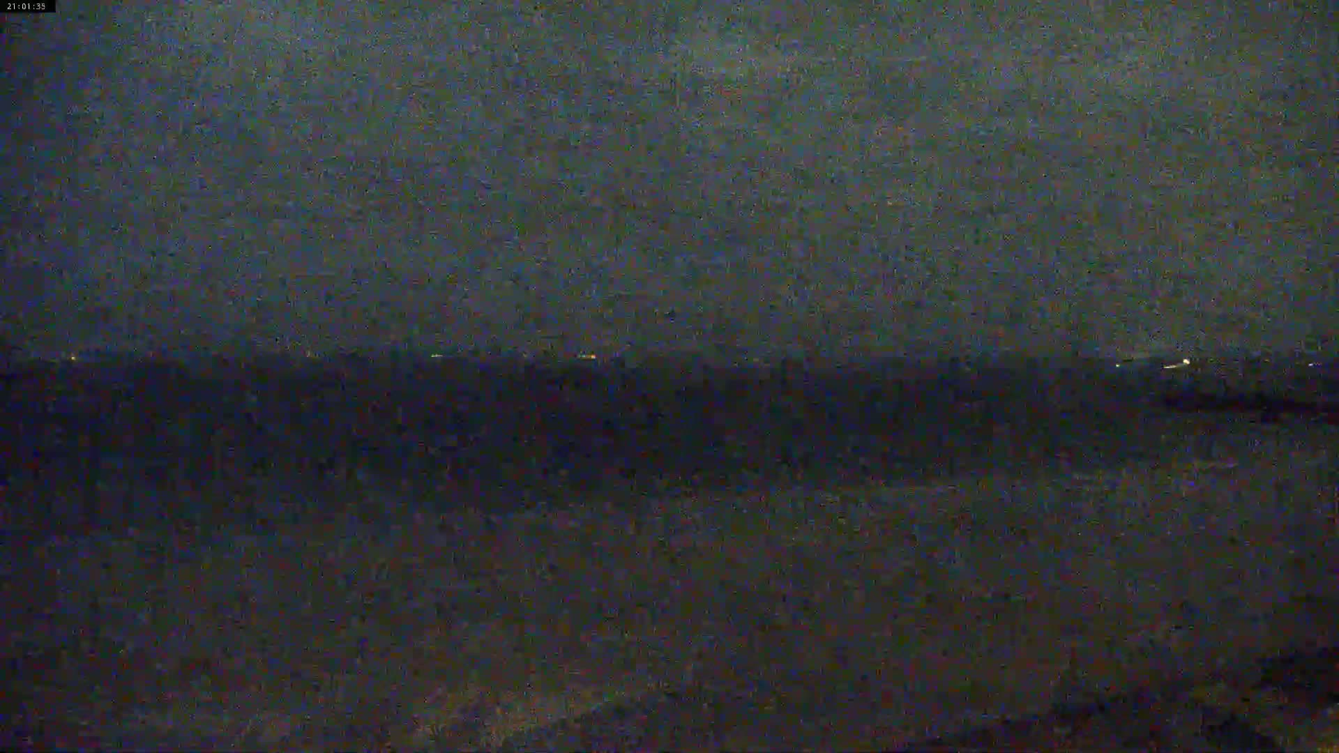 A dark, nighttime view of a calm body of water with a distant, faintly lit horizon.
