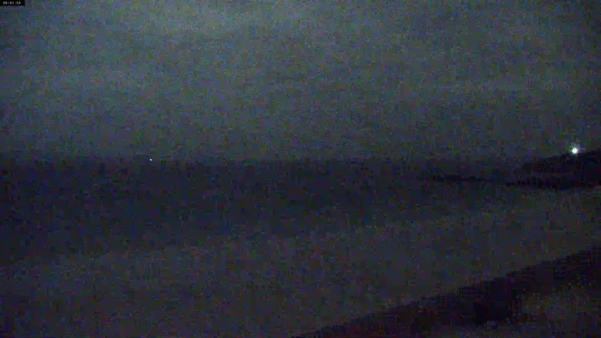 A dark, nighttime view of a calm body of water under a cloudy sky.