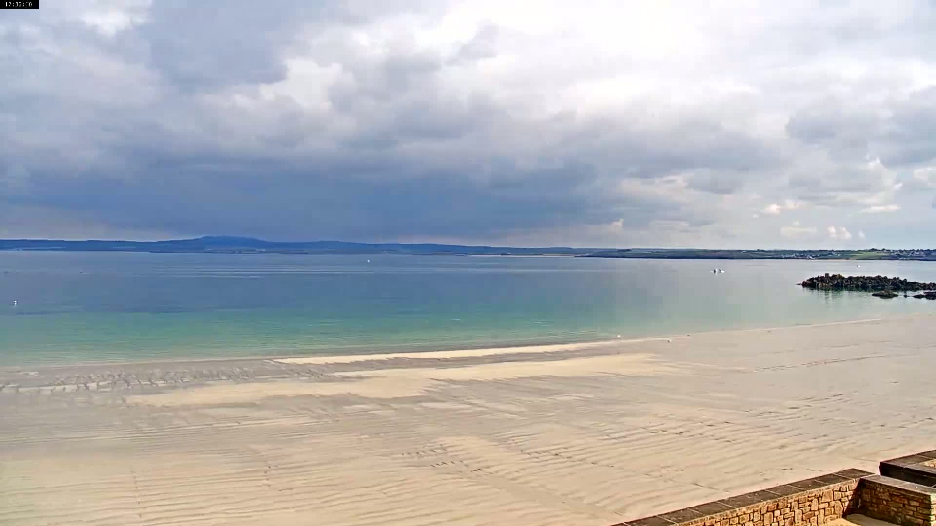 A wide, sandy beach stretches toward a calm body of water under a partly cloudy sky.