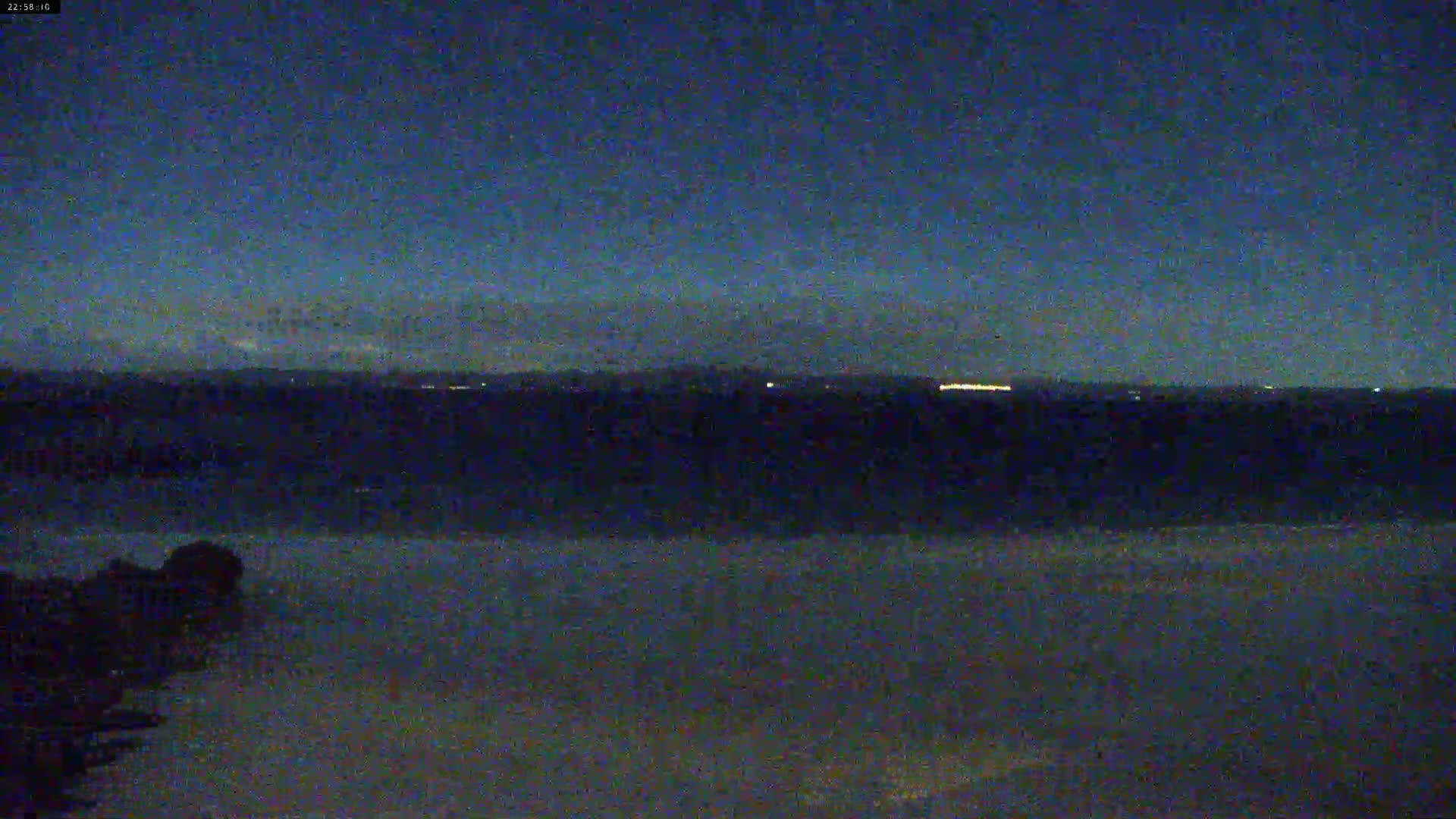 A dark, nighttime view of a body of water with a distant, faintly lit shoreline under a clear, dark sky.