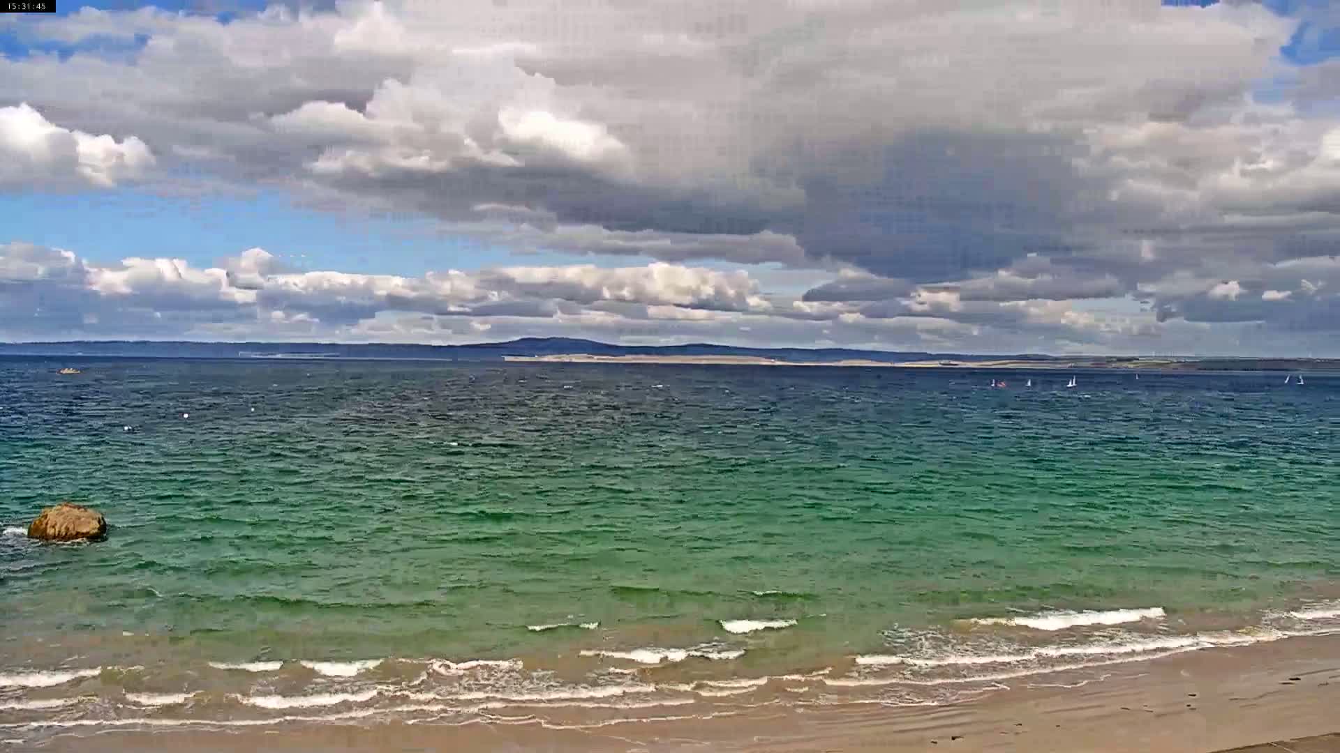 A partly cloudy sky hangs over a greenish-blue sea with small waves lapping a sandy beach.
