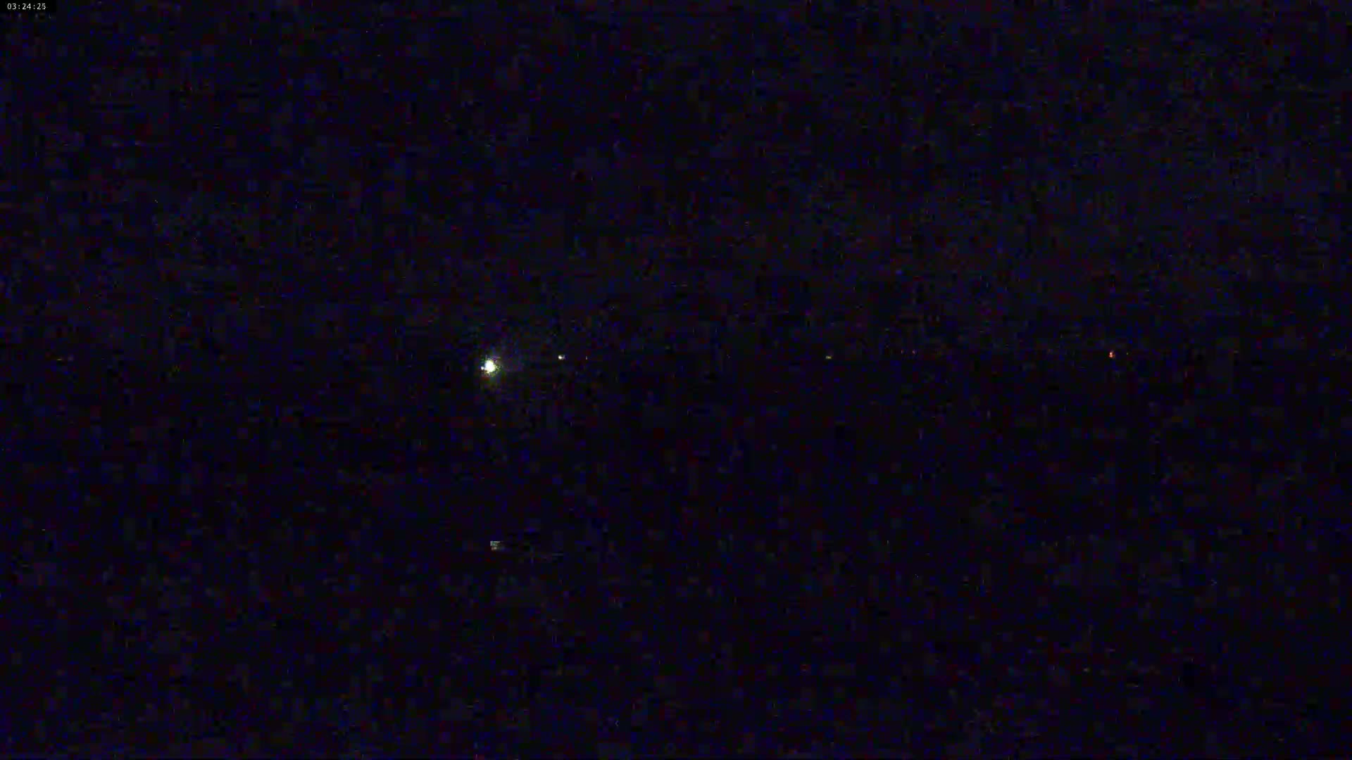 A dark night scene shows a few distant lights in the middle-ground and a brighter light to the left.