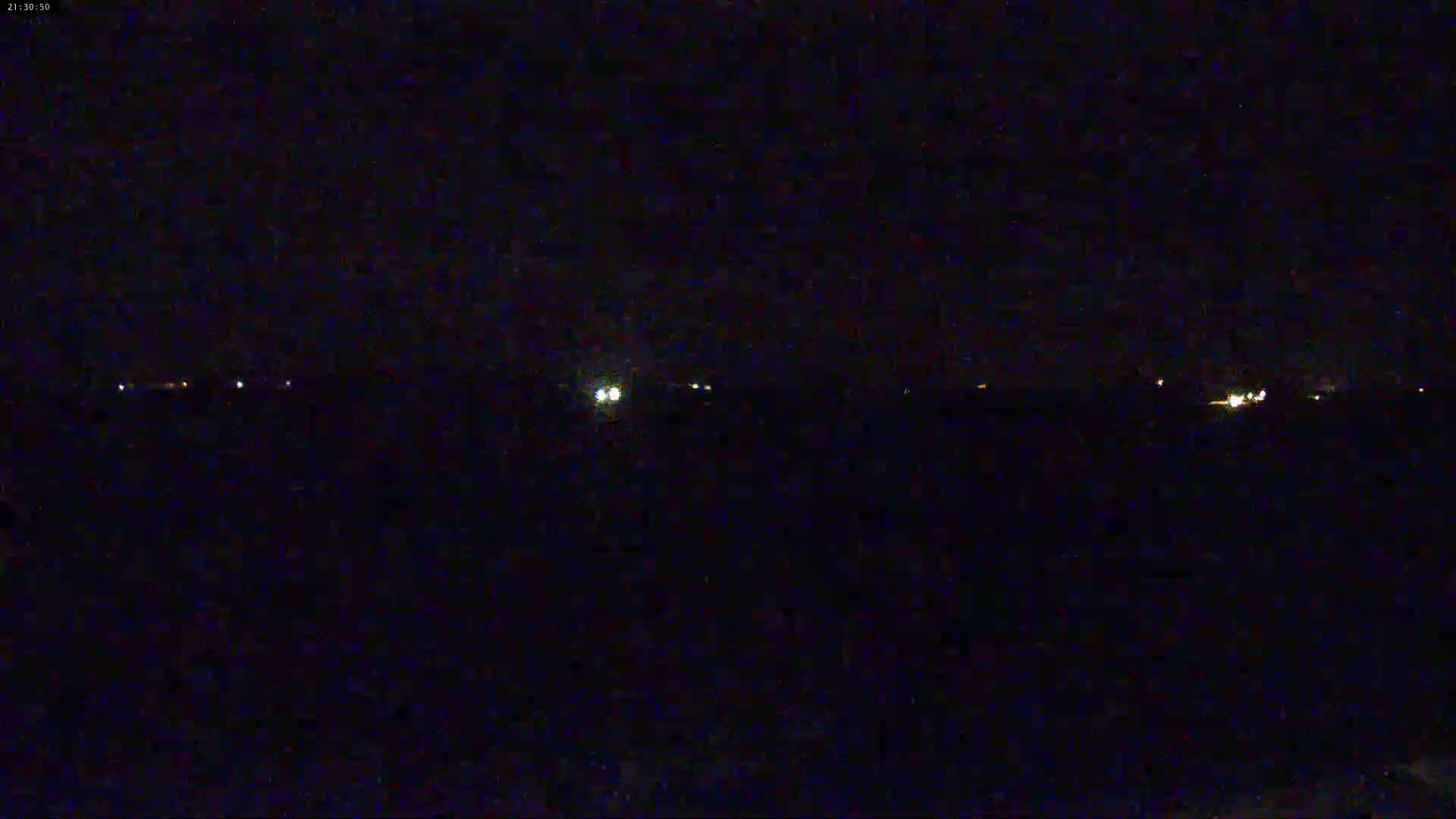 A dark nighttime scene shows a distant line of faint lights on the horizon under a clear sky.
