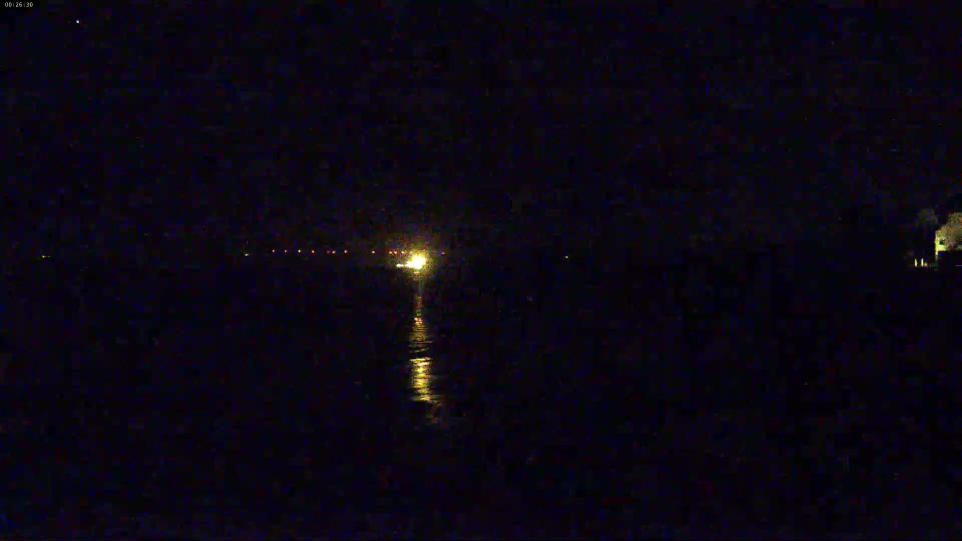 A bright light on the water at night is visible from a dark shore.