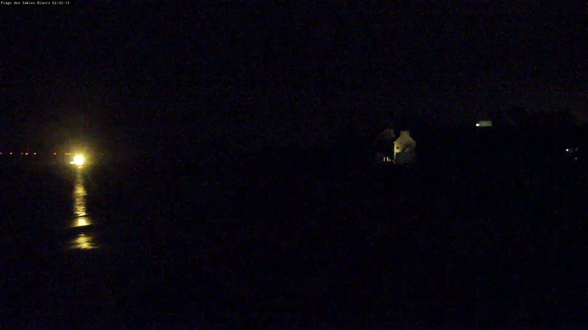 A bright light on the water is visible at night, with a dark shoreline and some dimly lit structures in the distance.