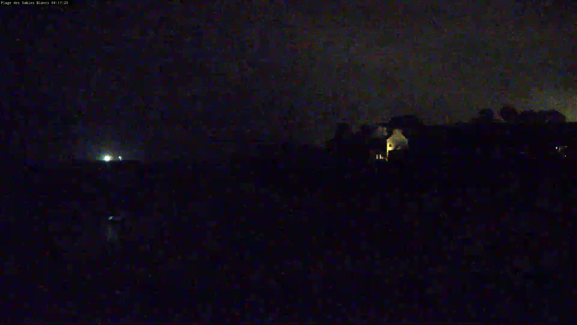 A nighttime, low-light view shows dark land with a few faintly lit buildings and a distant light source.