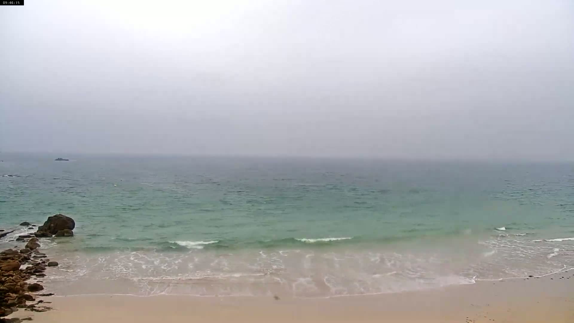 A sandy beach with small waves lapping the shore on a foggy day.
