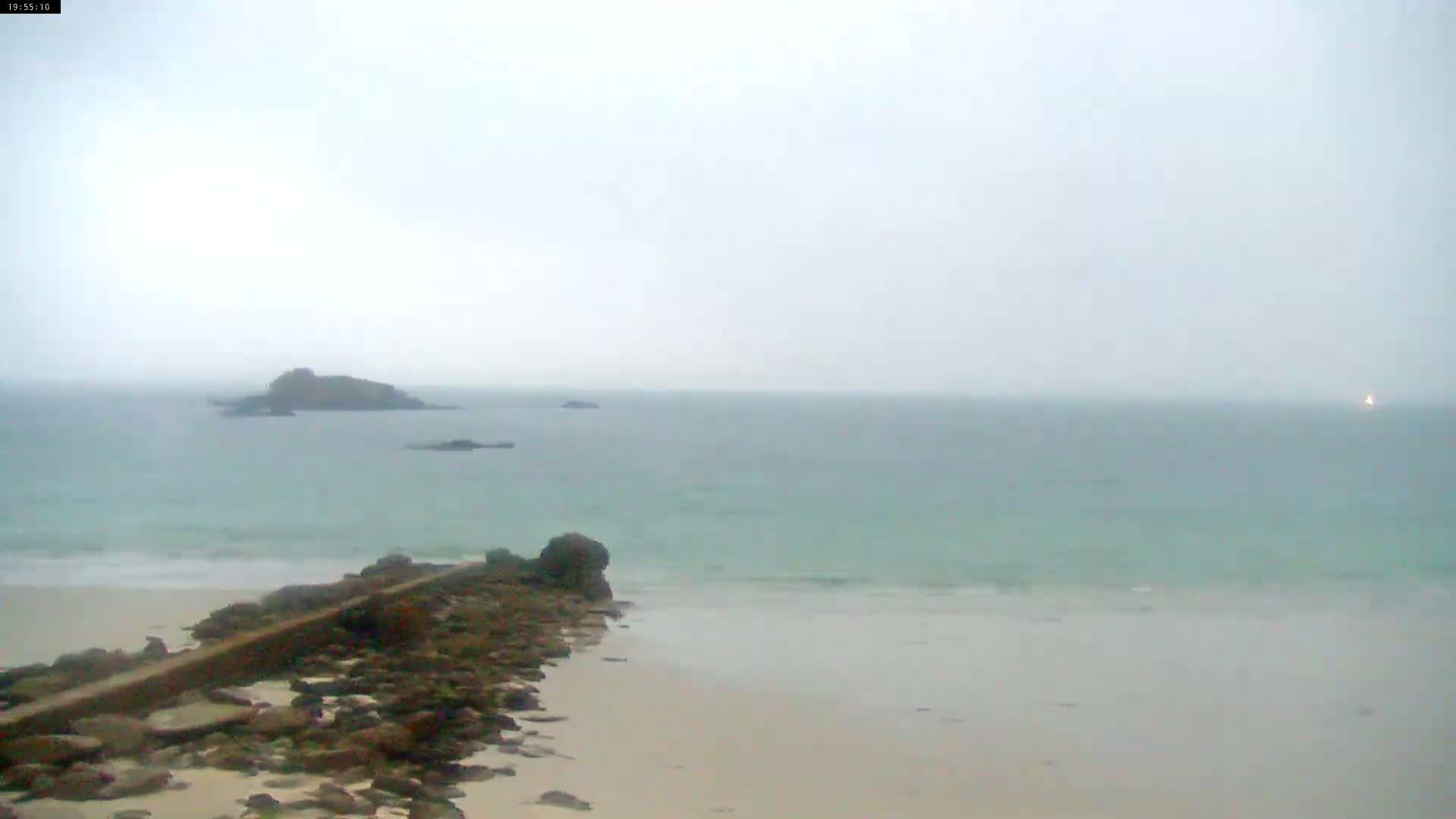 A rocky shoreline meets a calm, light-green sea under an overcast sky.