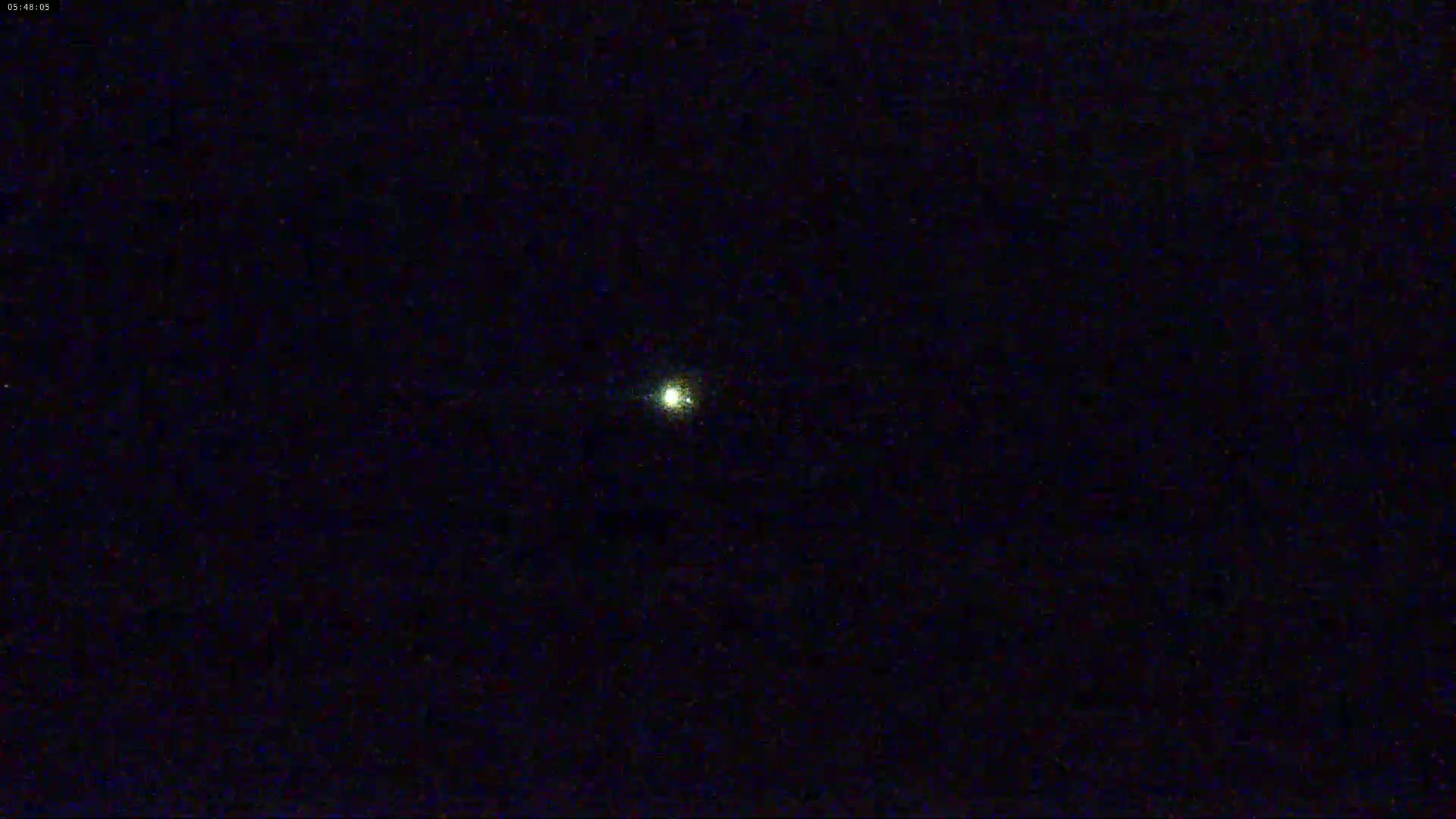 A single, bright light is visible in a dark, nighttime sky.