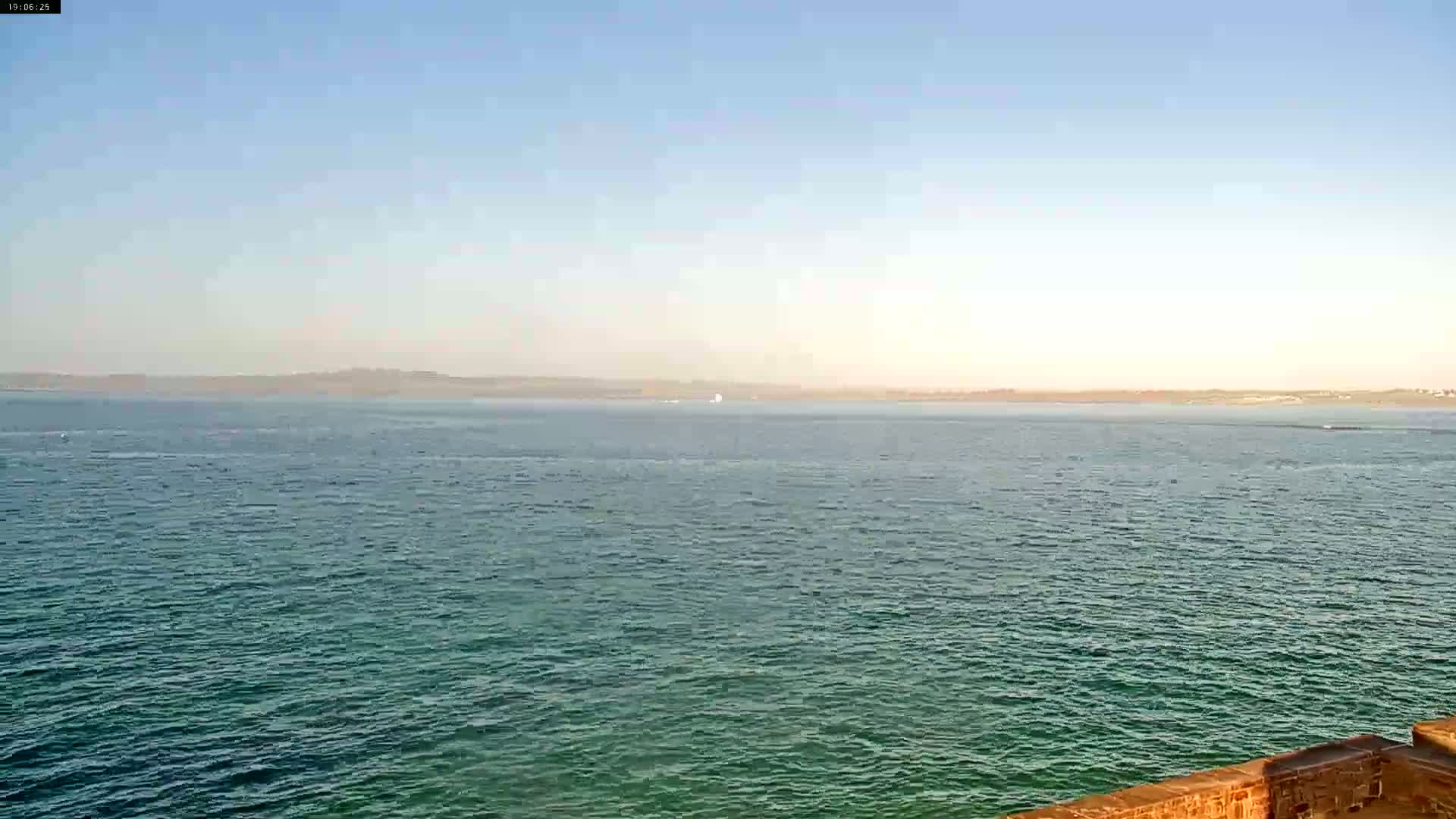 A calm, teal-colored body of water stretches to a hazy horizon under a clear, light-blue sky.
