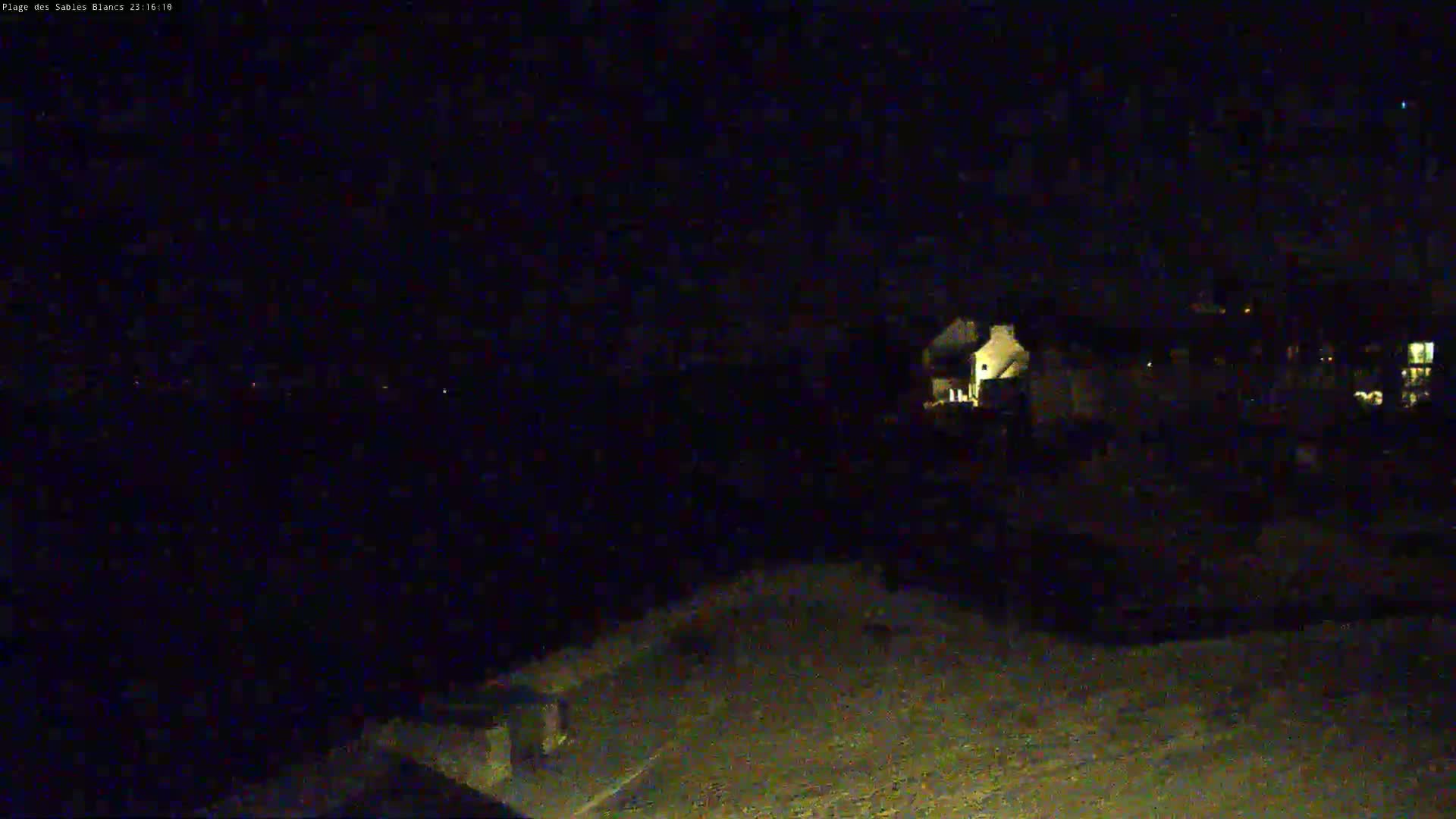 A nighttime, dark view of a few illuminated buildings from a distance, possibly overlooking a road.