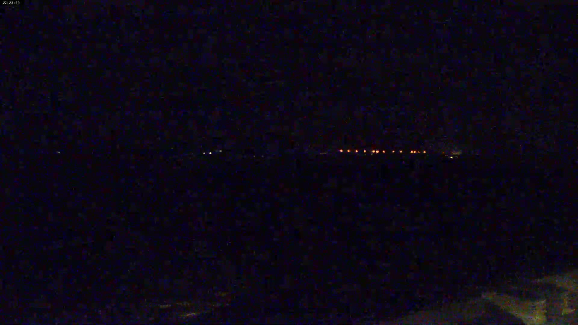 A dark, nighttime scene shows a distant line of orange lights on a horizon.