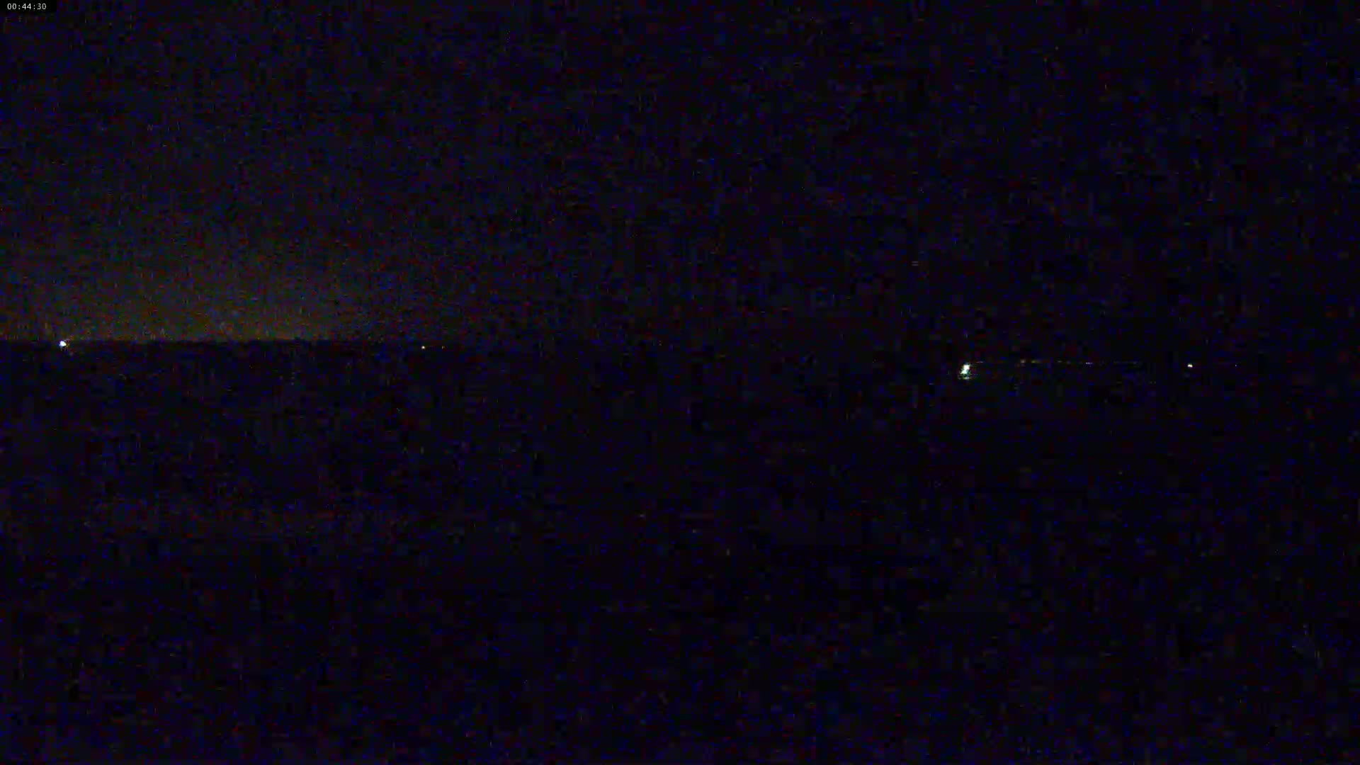 A dark, nighttime landscape is visible with a few faint lights on the horizon under a clear, dark sky.