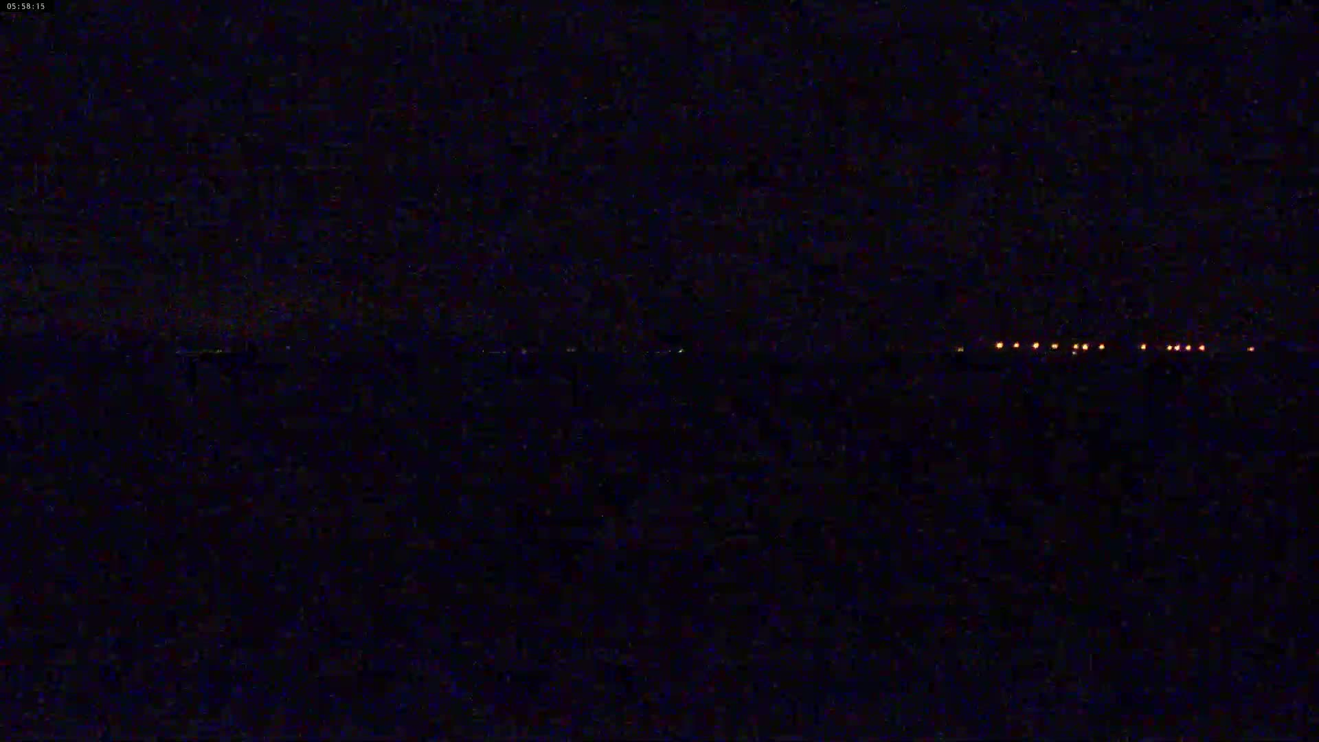 At night, a line of small, distant orange lights is visible on the horizon over a dark expanse.
