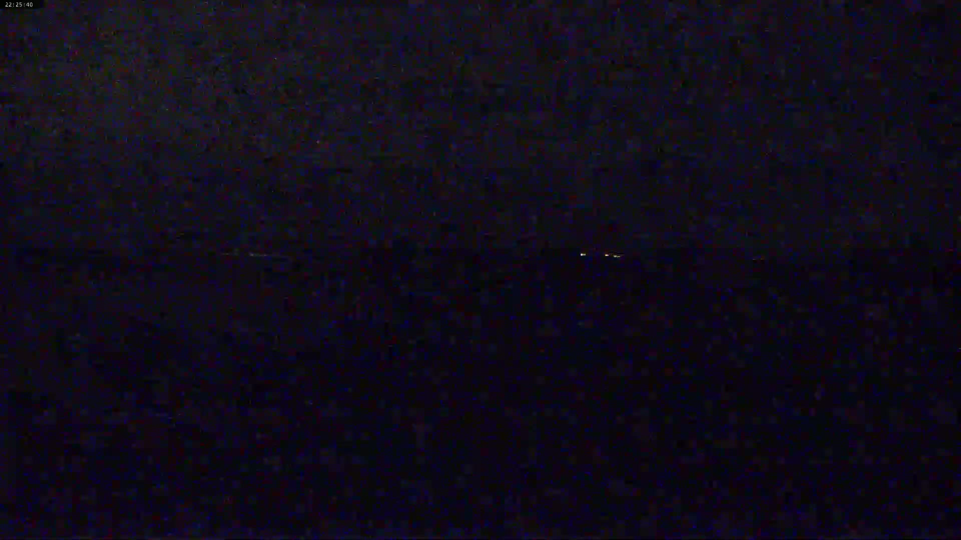 A dark, nighttime scene shows a faint line of lights on the horizon.