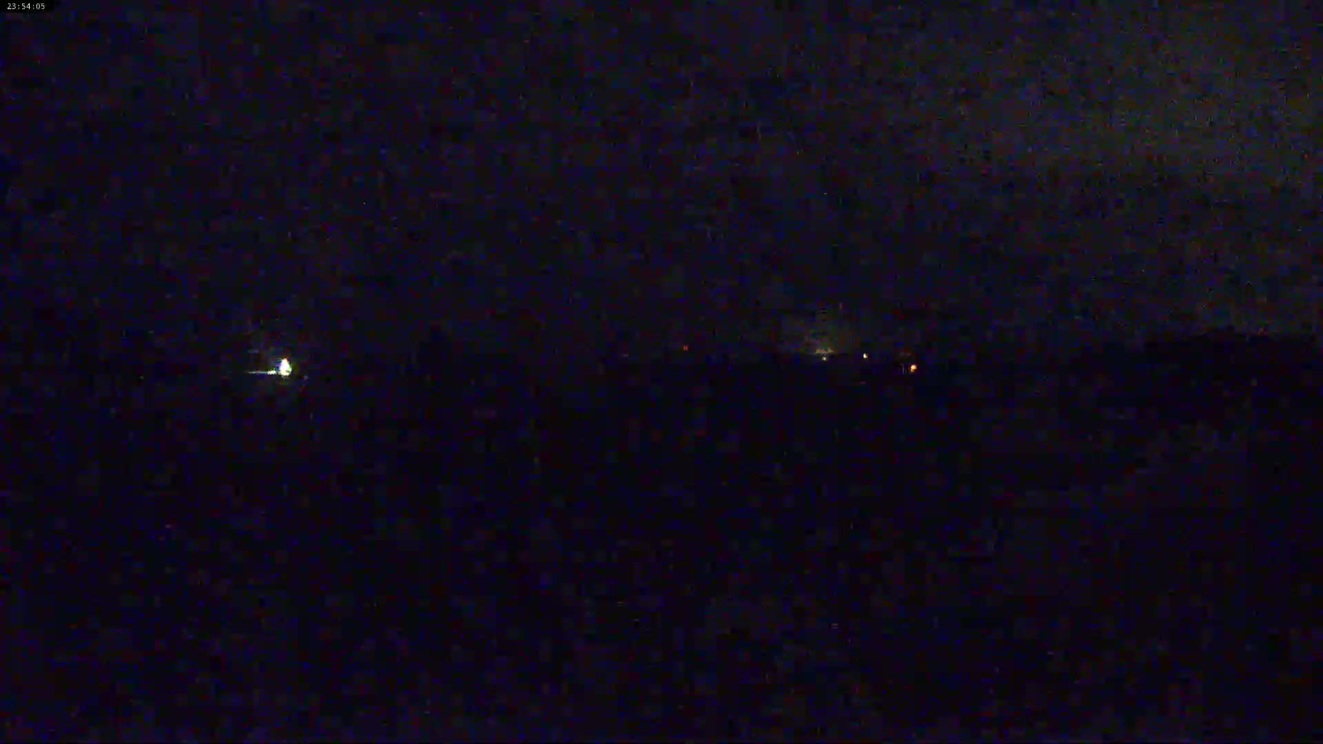 A dark, nighttime scene shows a few distant lights on the horizon under a mostly clear sky.