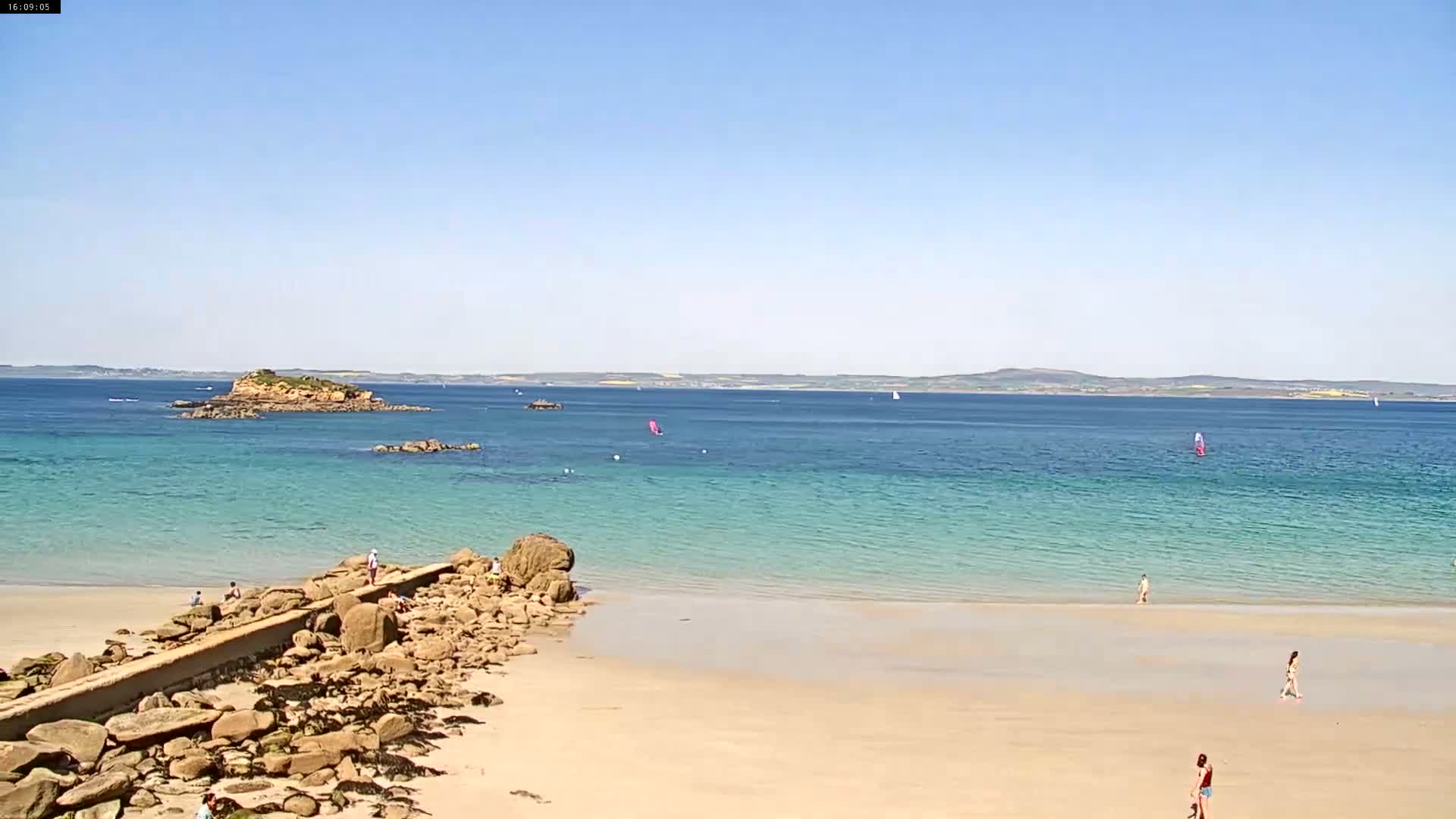 A sandy beach with turquoise water, rocky outcroppings, and several people enjoying a sunny day.