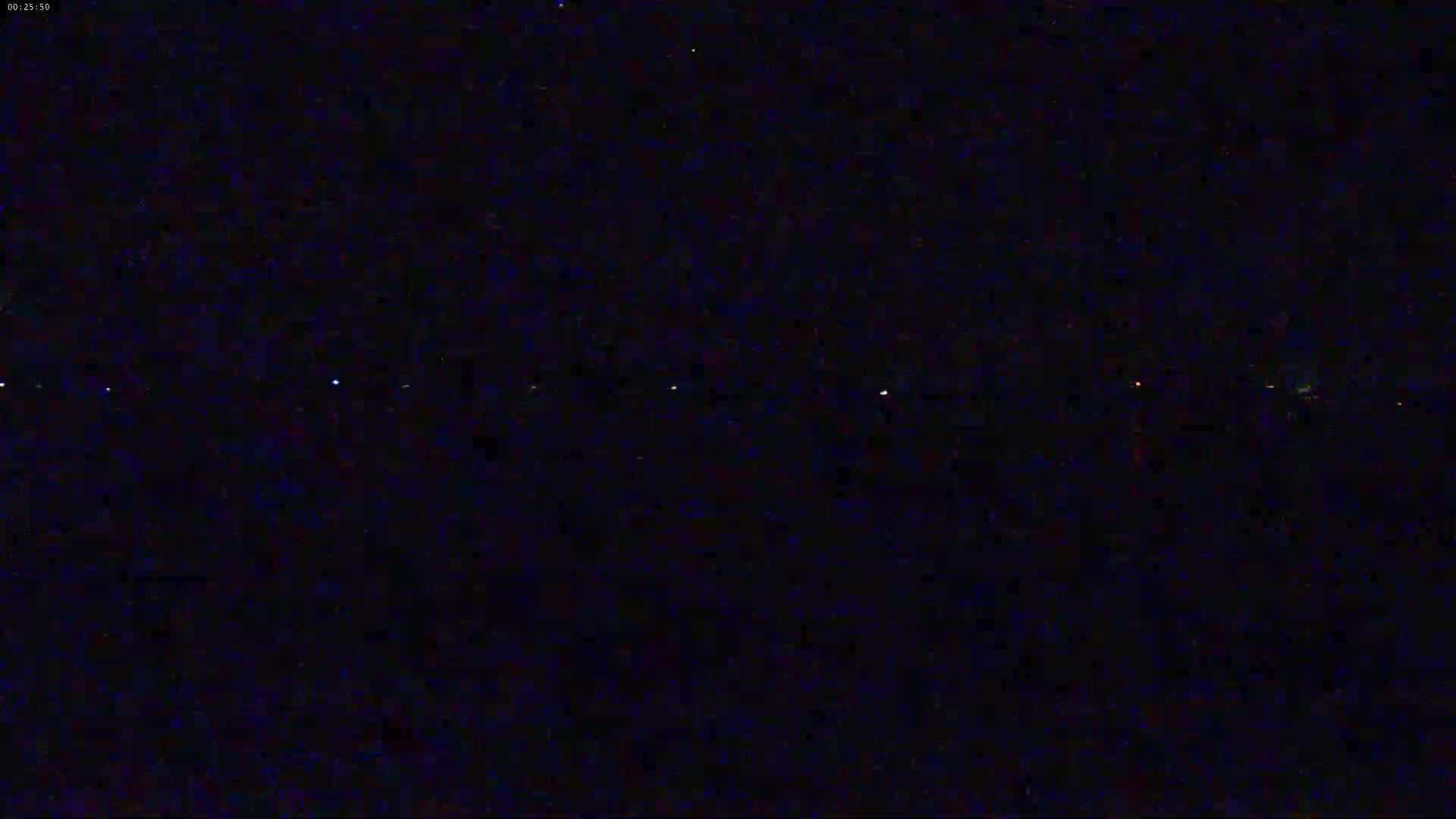 A dark, nighttime scene shows a faint line of distant lights on the horizon under a clear, starry sky.
