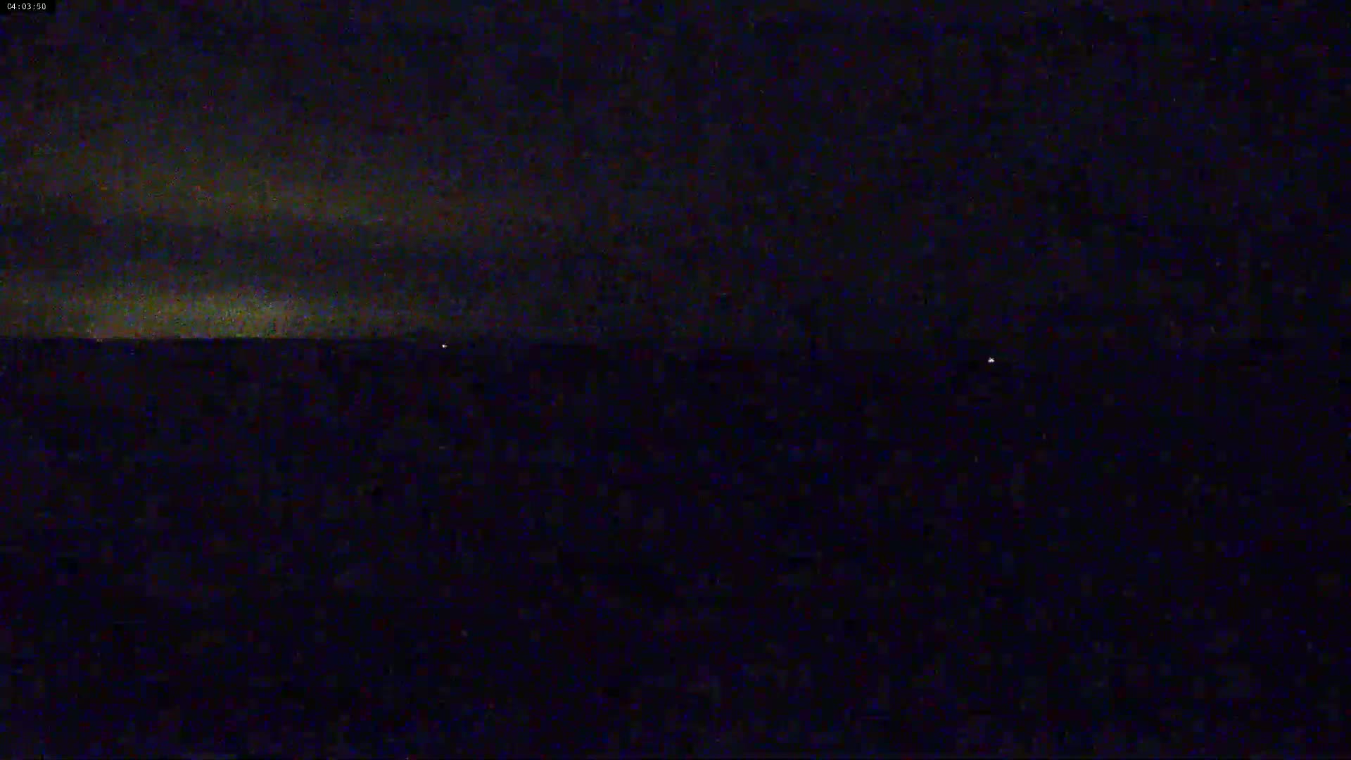 A dark, nighttime scene shows a flat, dark horizon under a cloudy sky.