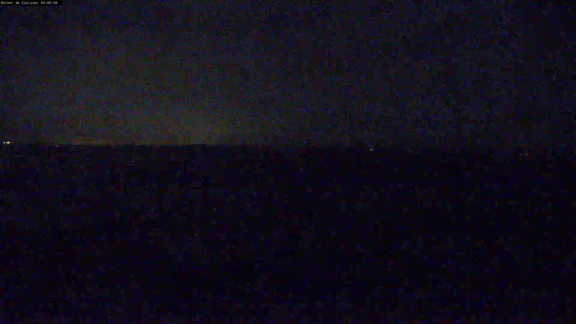 A dark, nighttime scene shows a flat, dark landscape under a mostly clear, dark sky.