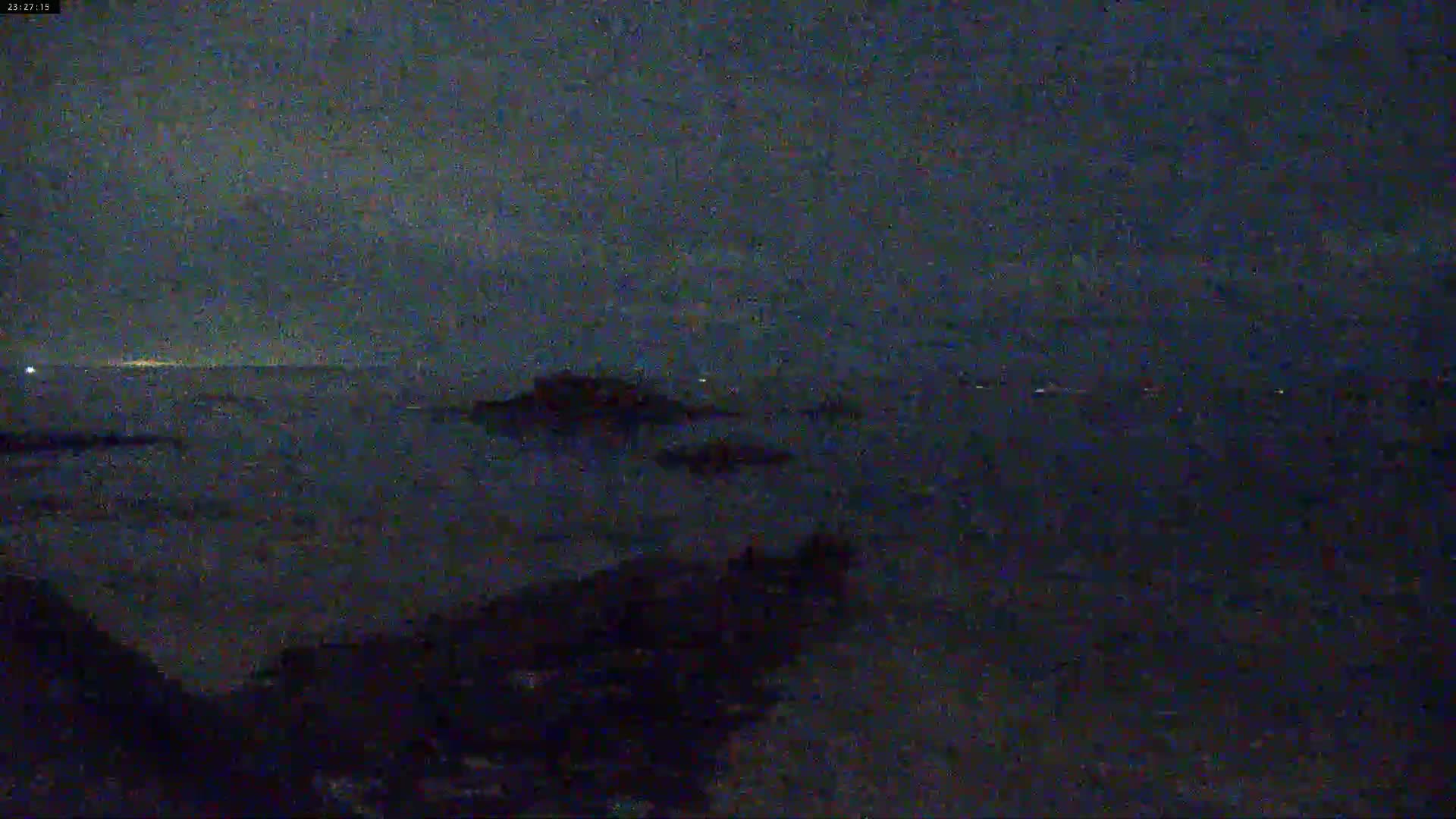 A nighttime, dark view of a body of water with some landmasses in the distance under a cloudy sky.