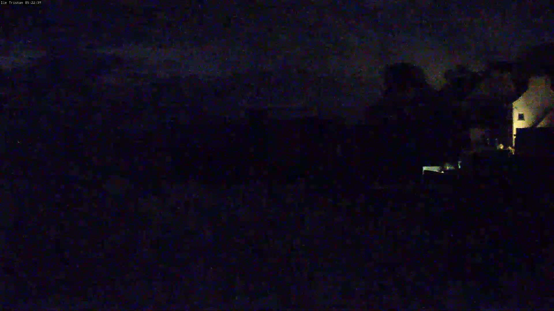 A dark, nighttime scene shows dimly lit buildings under a cloudy sky.