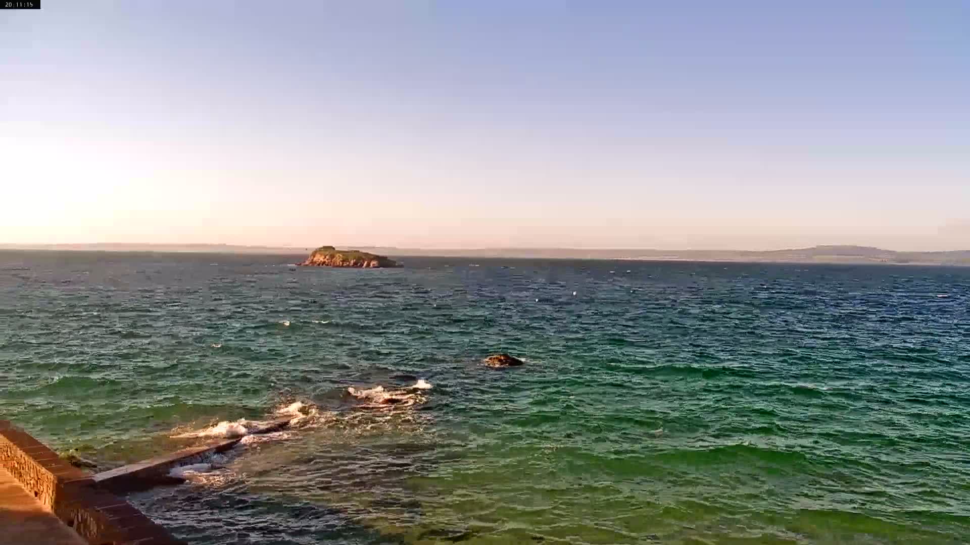 A small island is visible in the distance across a body of teal water with small waves under a clear, light blue sky.