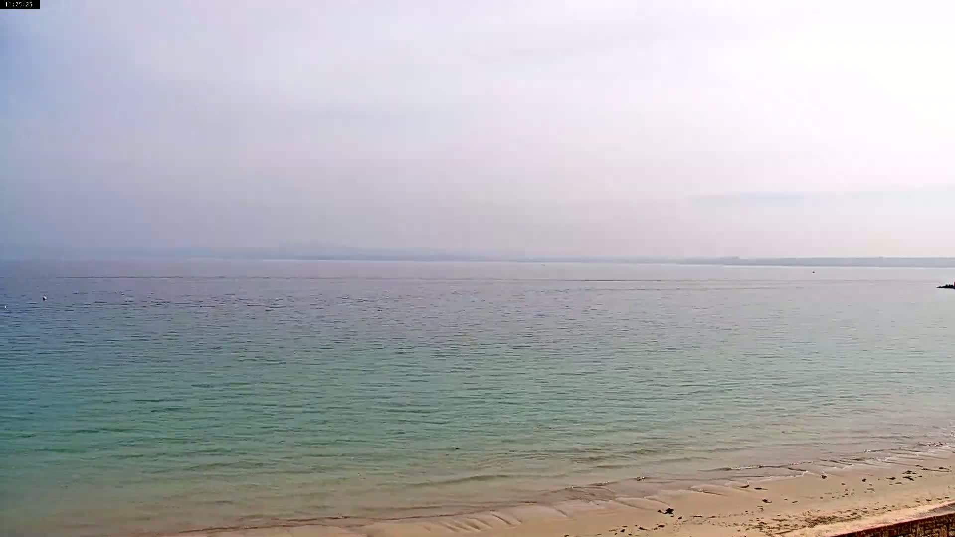 A calm, hazy ocean meets a sandy beach.