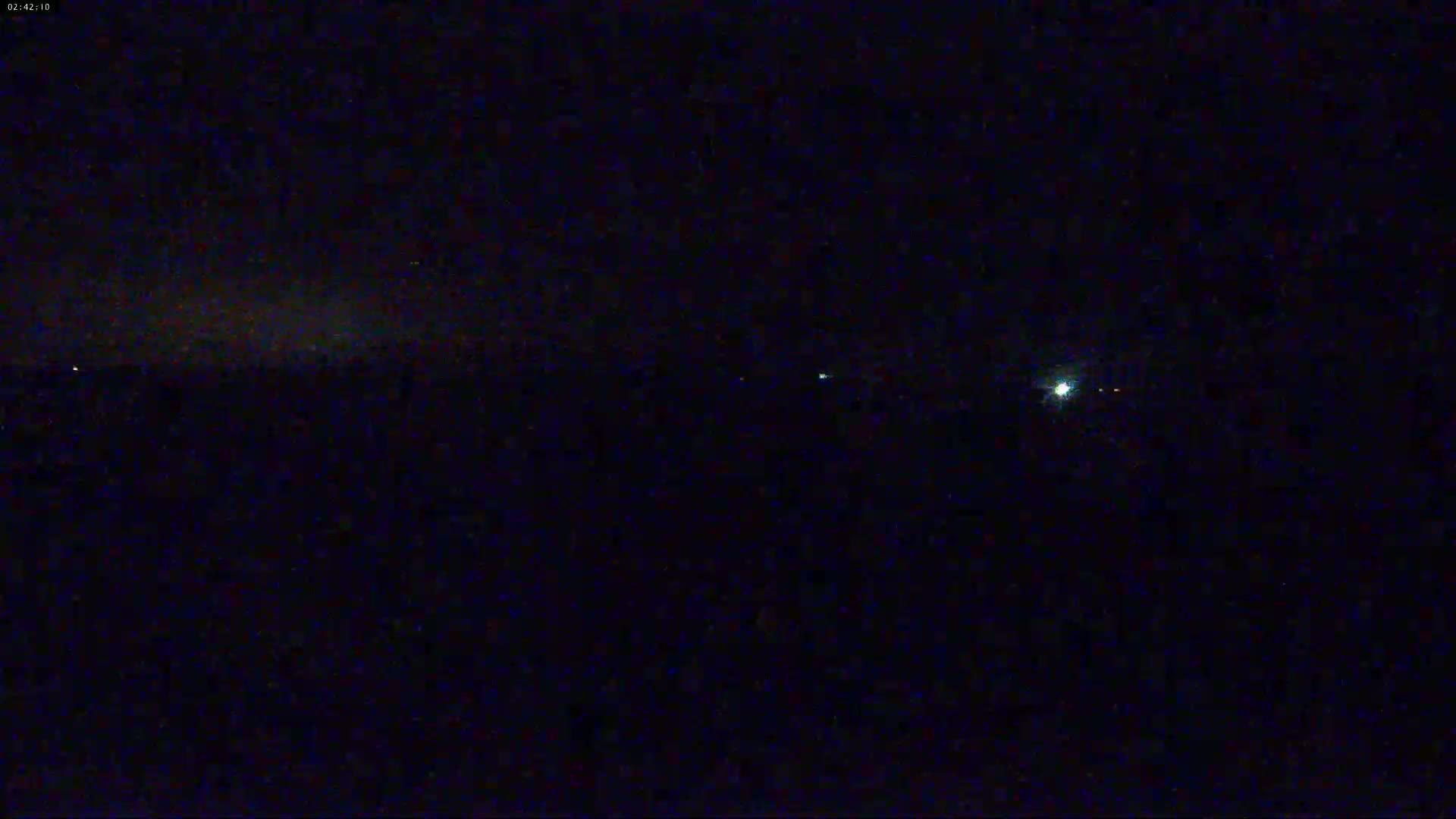 A dark, nighttime scene shows a few faint lights in the distance under a mostly clear sky.