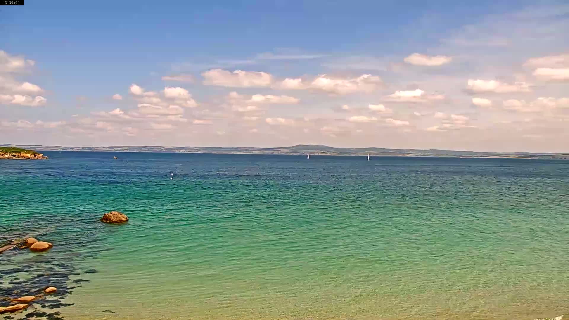 A calm, clear body of teal water stretches to a distant landmass under a partly cloudy sky.