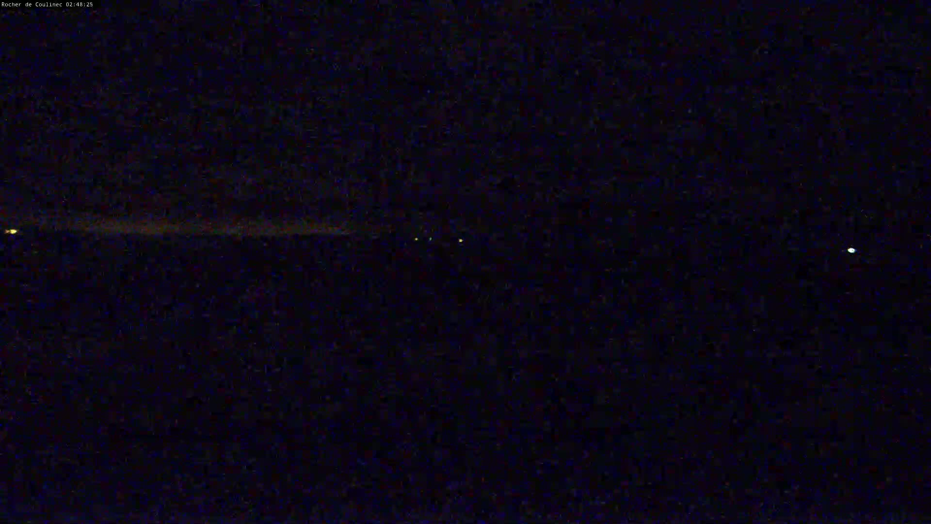 A nighttime long shot shows a dark landscape with a few faint lights in the distance under a clear, dark sky.
