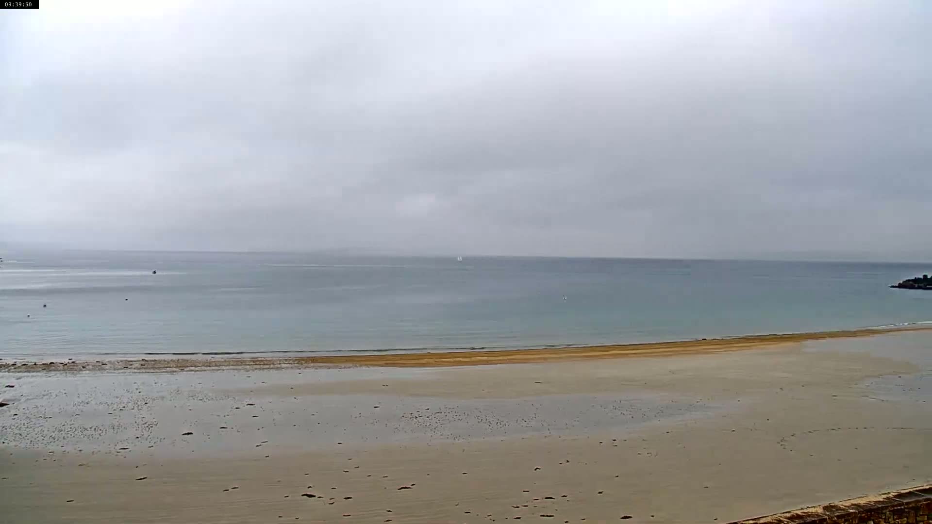 A wide sandy beach stretches out to a calm, gray-toned ocean under an overcast sky.