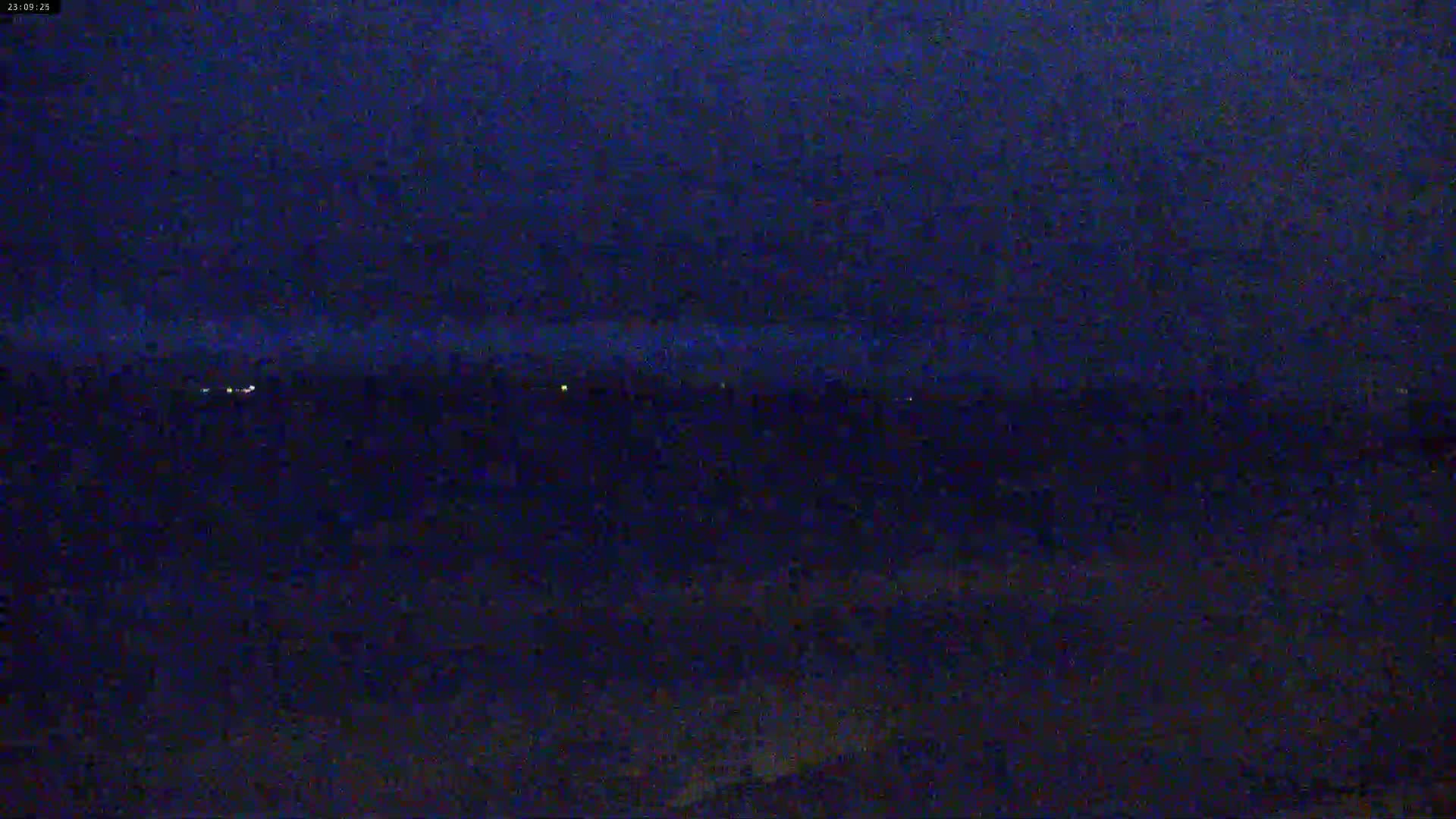 A dark, nighttime landscape is visible with a few distant lights on the horizon under a mostly clear, dark sky.