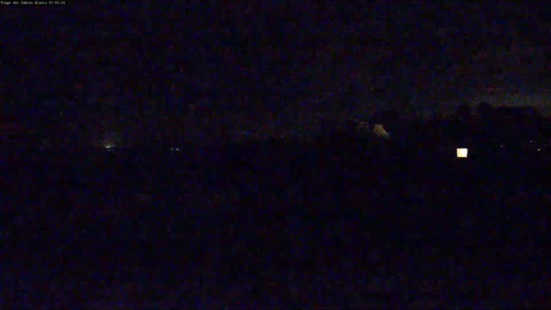 A dark, nighttime scene shows a few faint lights in the distance under a mostly clear sky.