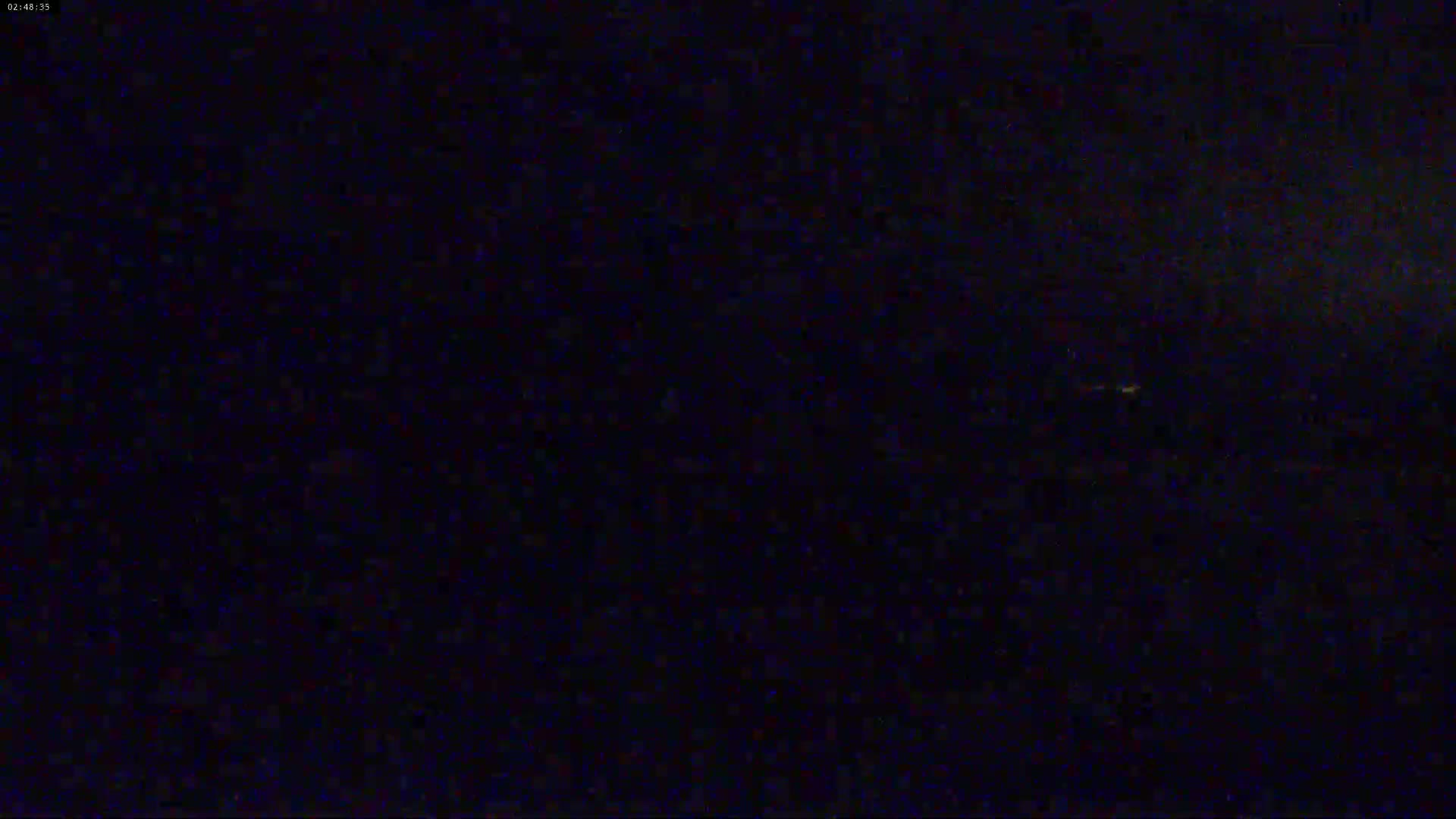 The image shows a dark, nighttime scene with a few faint, distant lights visible.