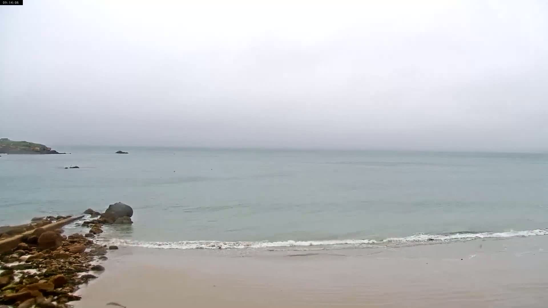 A rocky shoreline meets a calm, light-blue sea under an overcast sky.