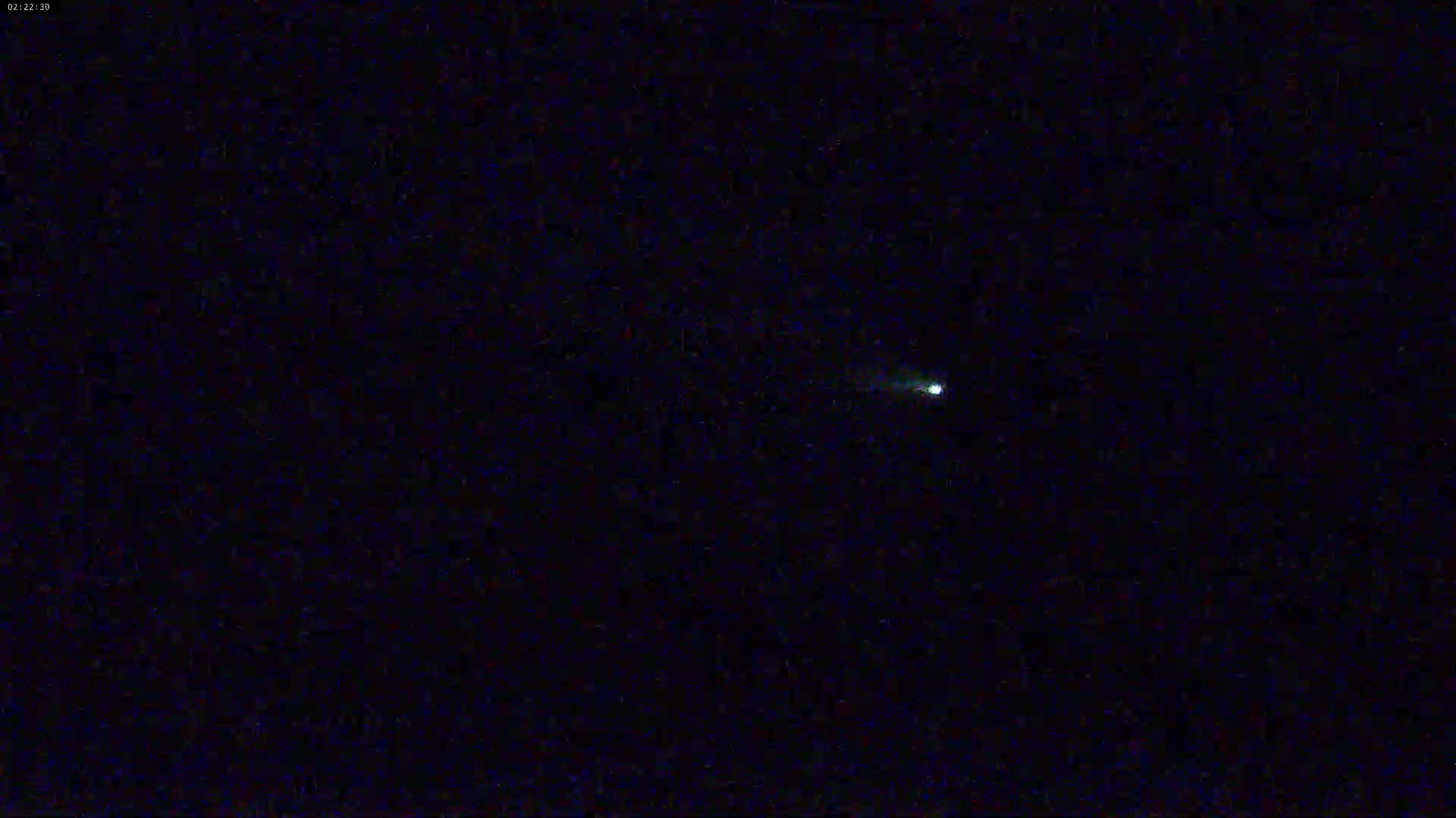 A small, bright light is visible in a dark night sky.