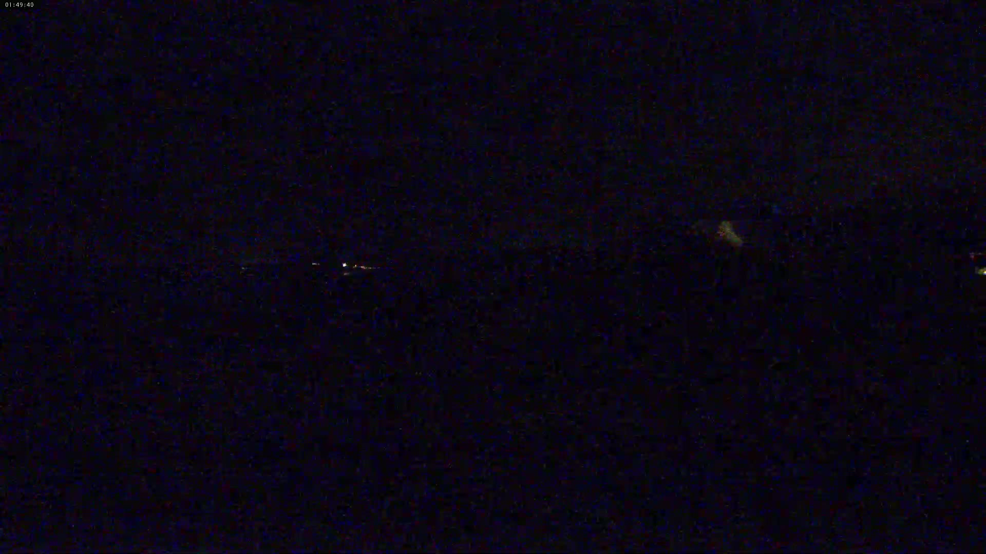 A nighttime, dark landscape is visible with a few distant, faint lights.
