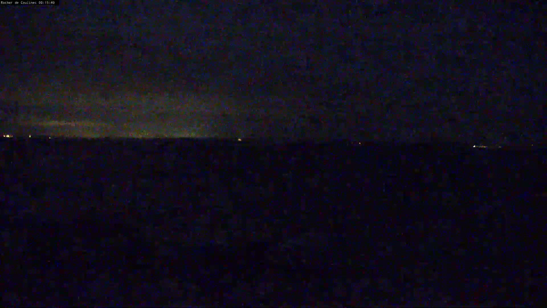 A dark, nighttime view of a body of water with a faint horizon line and distant, small lights.