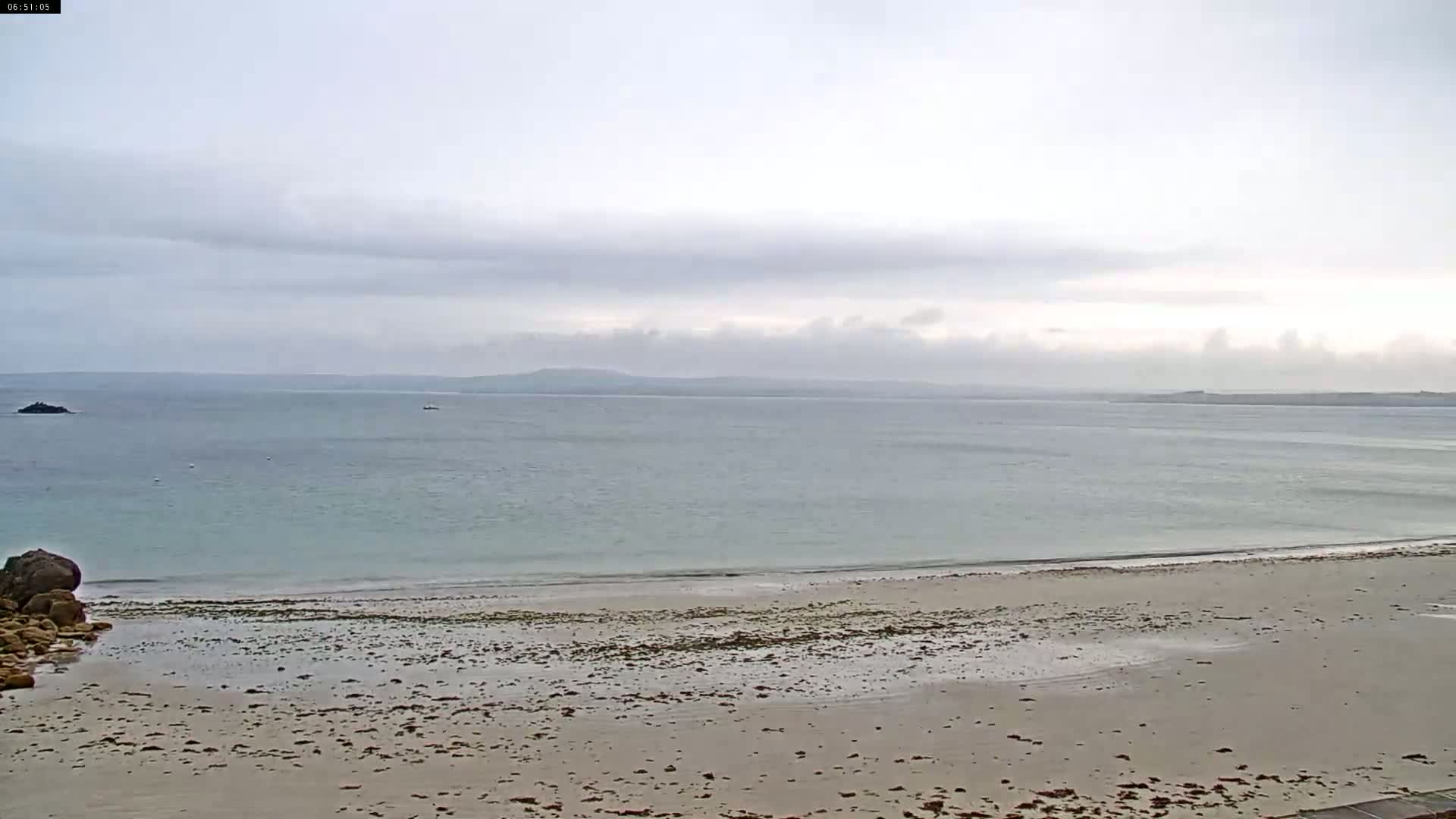 A sandy beach stretches to a calm, light-blue sea under a cloudy sky.