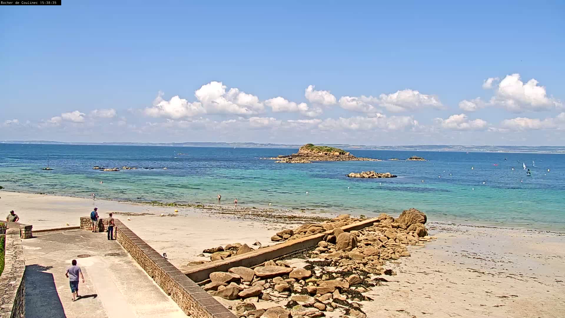 A sandy beach with turquoise water and a small island in the distance under a partly cloudy sky.