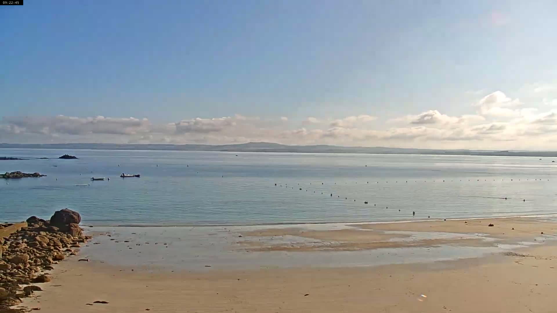 A sandy beach stretches to a calm, light-blue ocean under a mostly clear sky with scattered clouds.