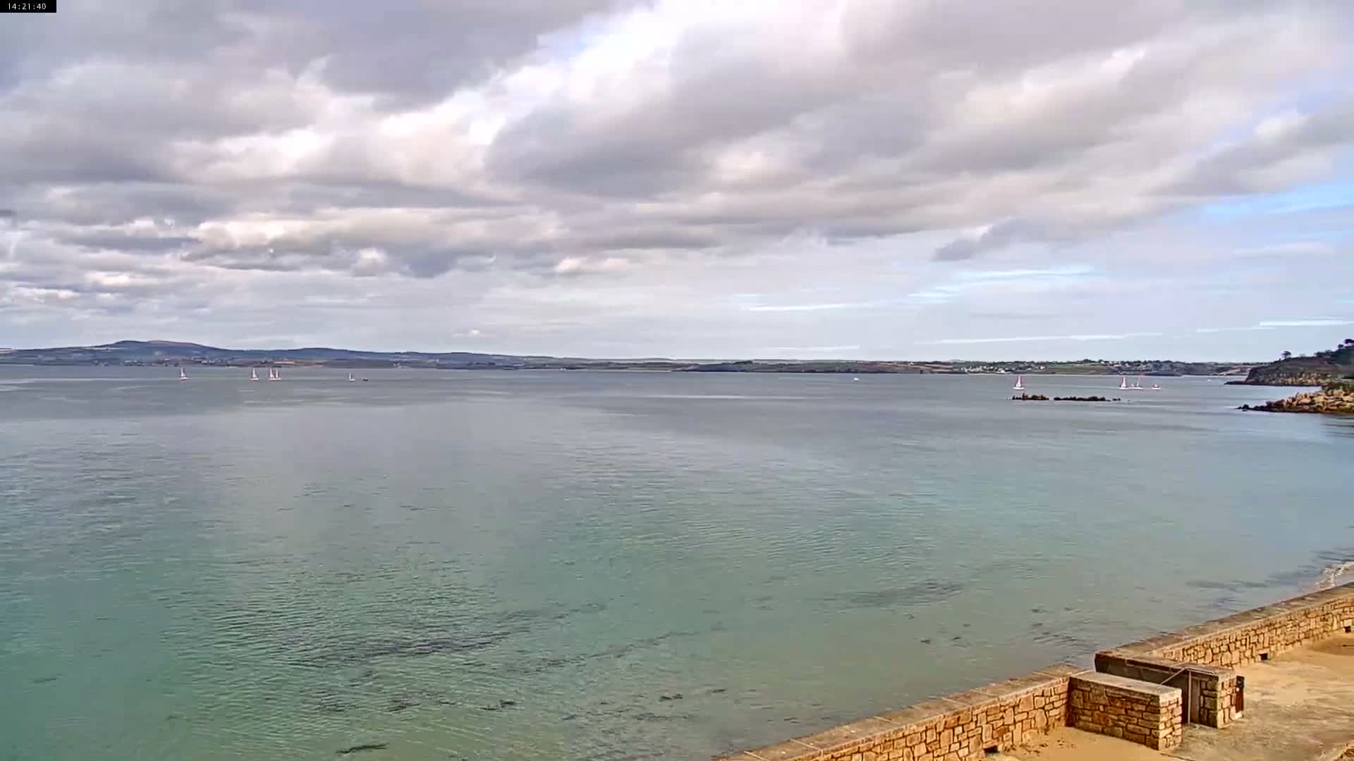 Three sailboats are on a sandy beach next to calm water under a cloudy sky.