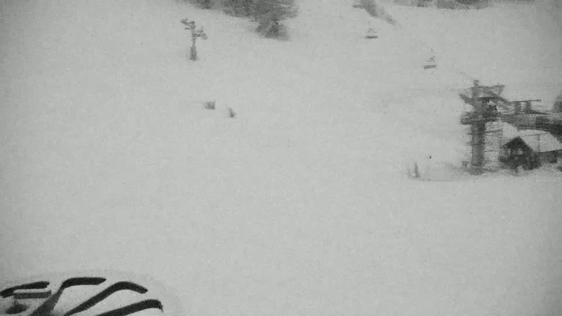 A snowy ski slope with several chairlifts and a small building is visible in the snow, under heavy snowfall.