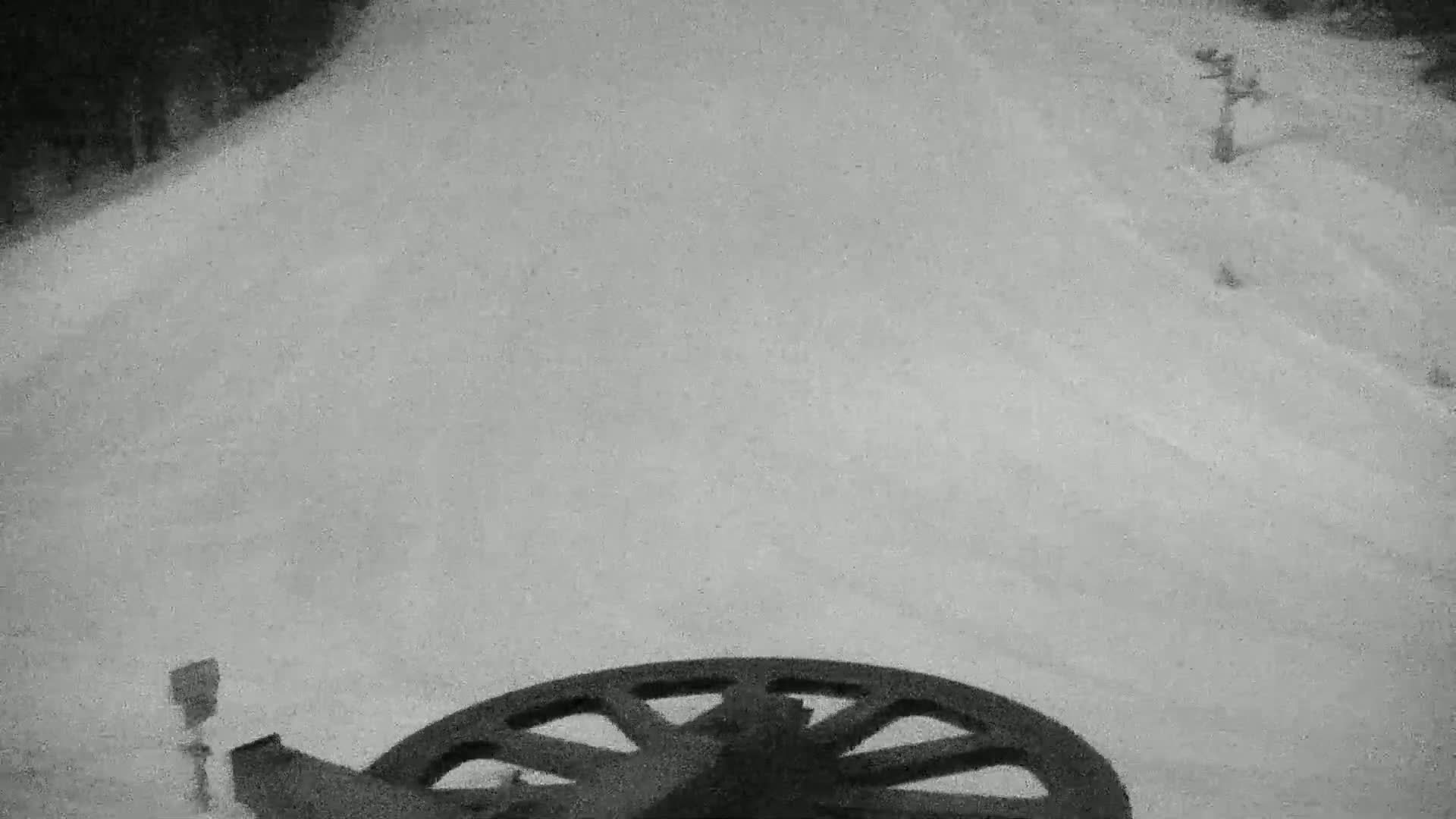 A large, dark-colored wheel is visible in the lower portion of a snowy, overcast scene.