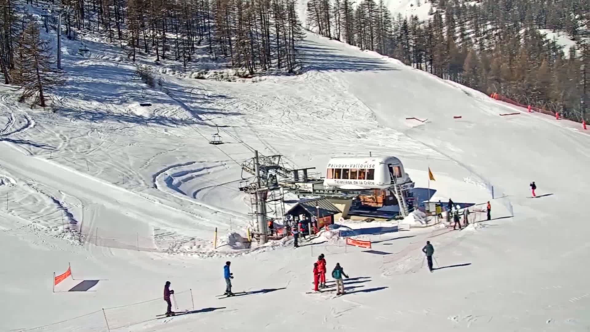 A ski slope with a chairlift and several skiers and snowboarders on a sunny day.